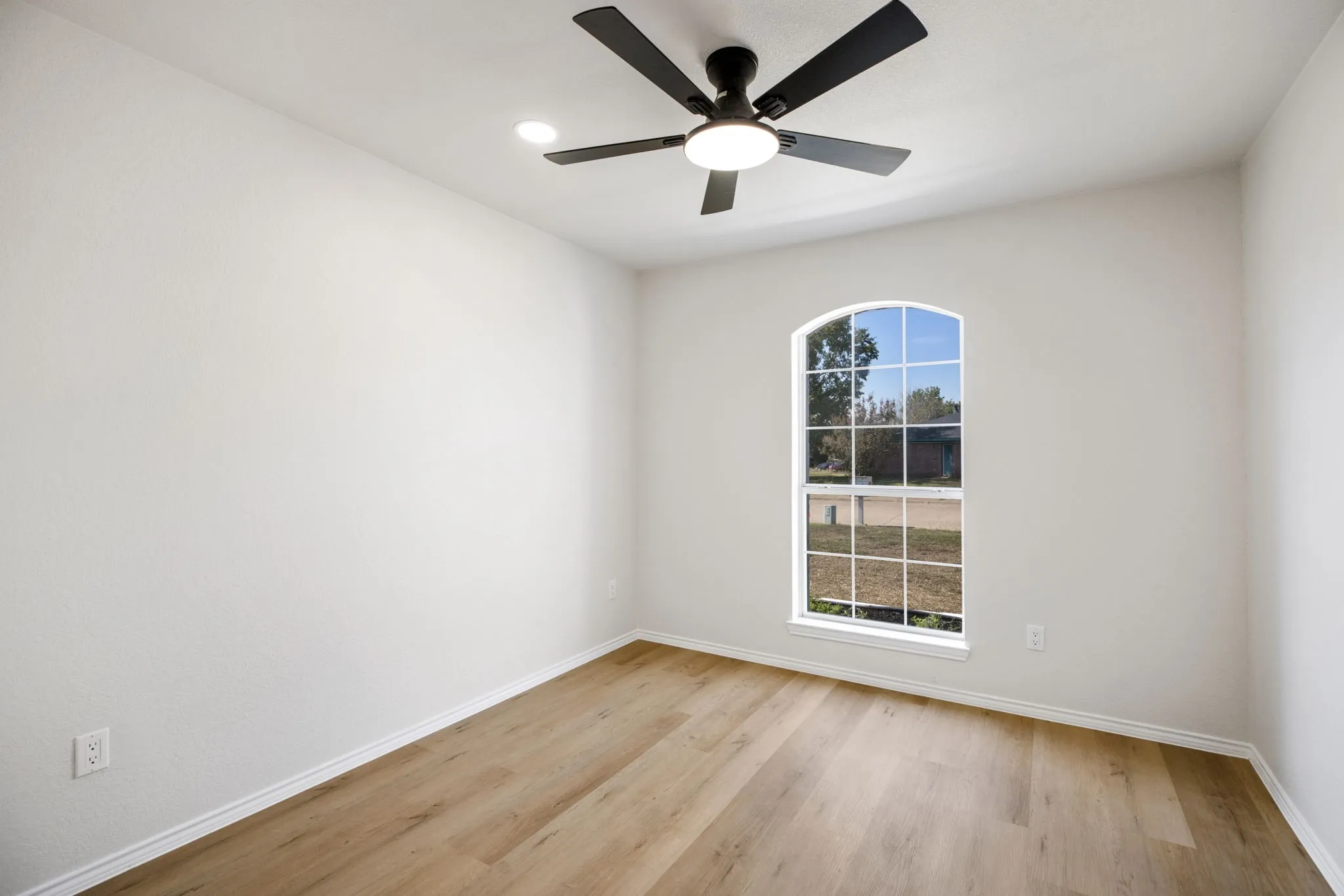 Arched window with white framing, wood-finish flooring, ceiling fan with integrated lighting, and white walls