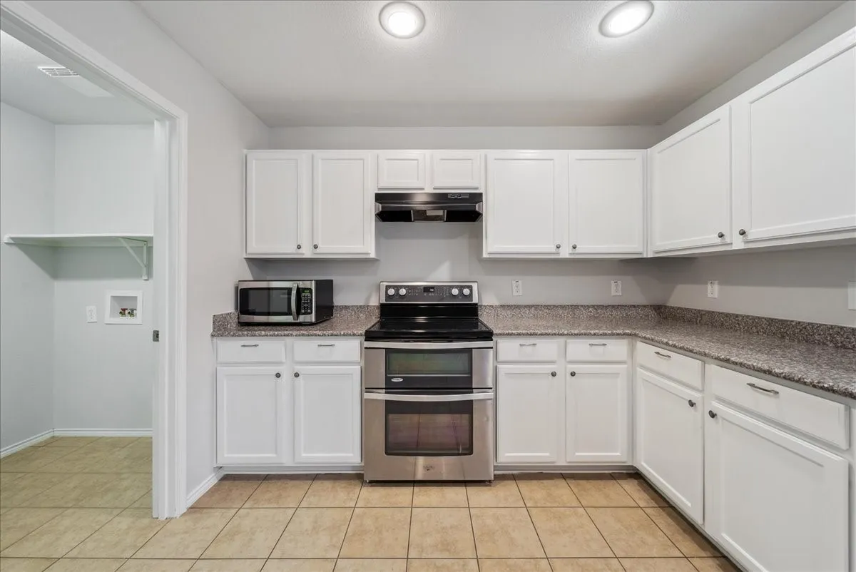 Kitchen featuring white cabinetry, stone-look countertops, stainless steel appliances, and tile flooring