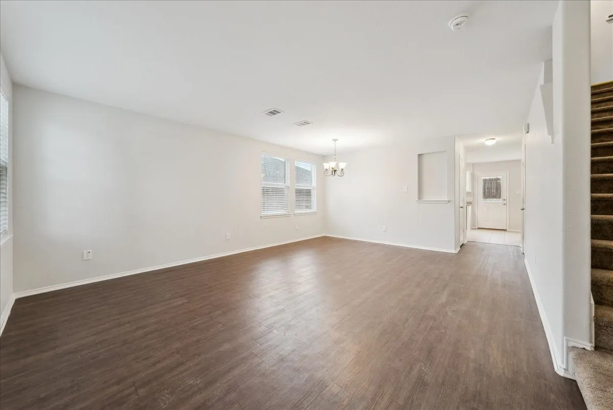 Expansive open-concept living area with wood-finish flooring, multiple windows, and a chandelier