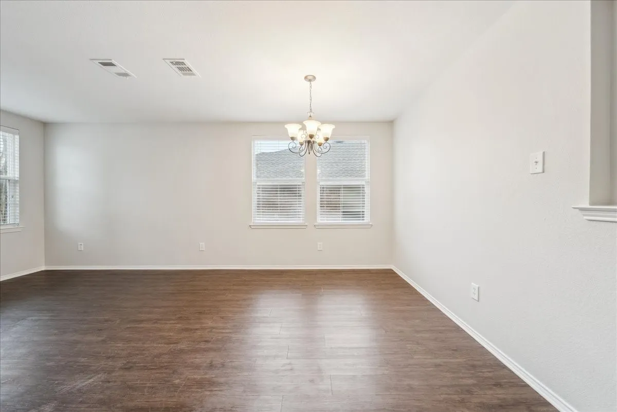 Spacious room featuring wood-finish flooring, white walls, and multiple windows with blinds