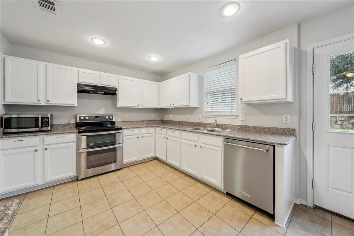 White cabinetry, granite-finish countertops, stainless steel appliances, recessed lighting, and tile flooring