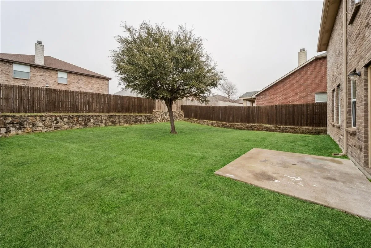 Expansive grass lawn featuring a mature tree, privacy fencing, and stone retaining walls