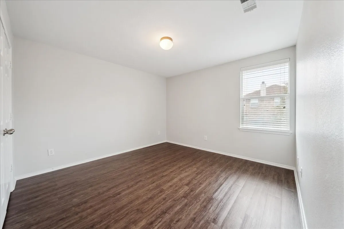 Spacious room featuring wood-finish flooring, neutral-toned walls, and a window with blinds
