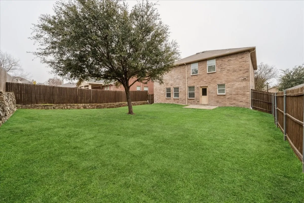 Expansive green lawn with a mature tree, stone retaining wall, and wood privacy fencing