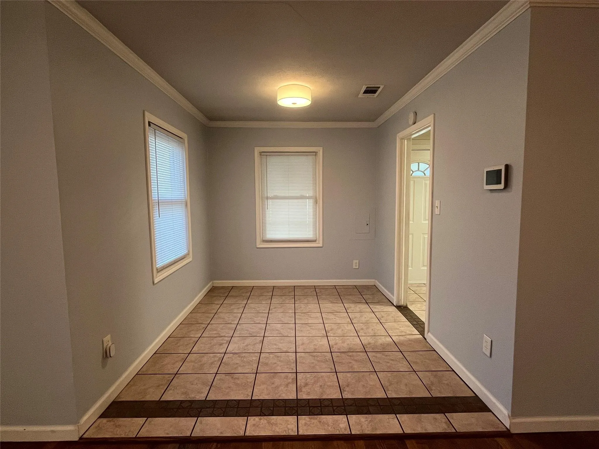 Ceramic tile flooring with a decorative inlay, two windows with blinds, crown molding, and a flush mount ceiling fixture