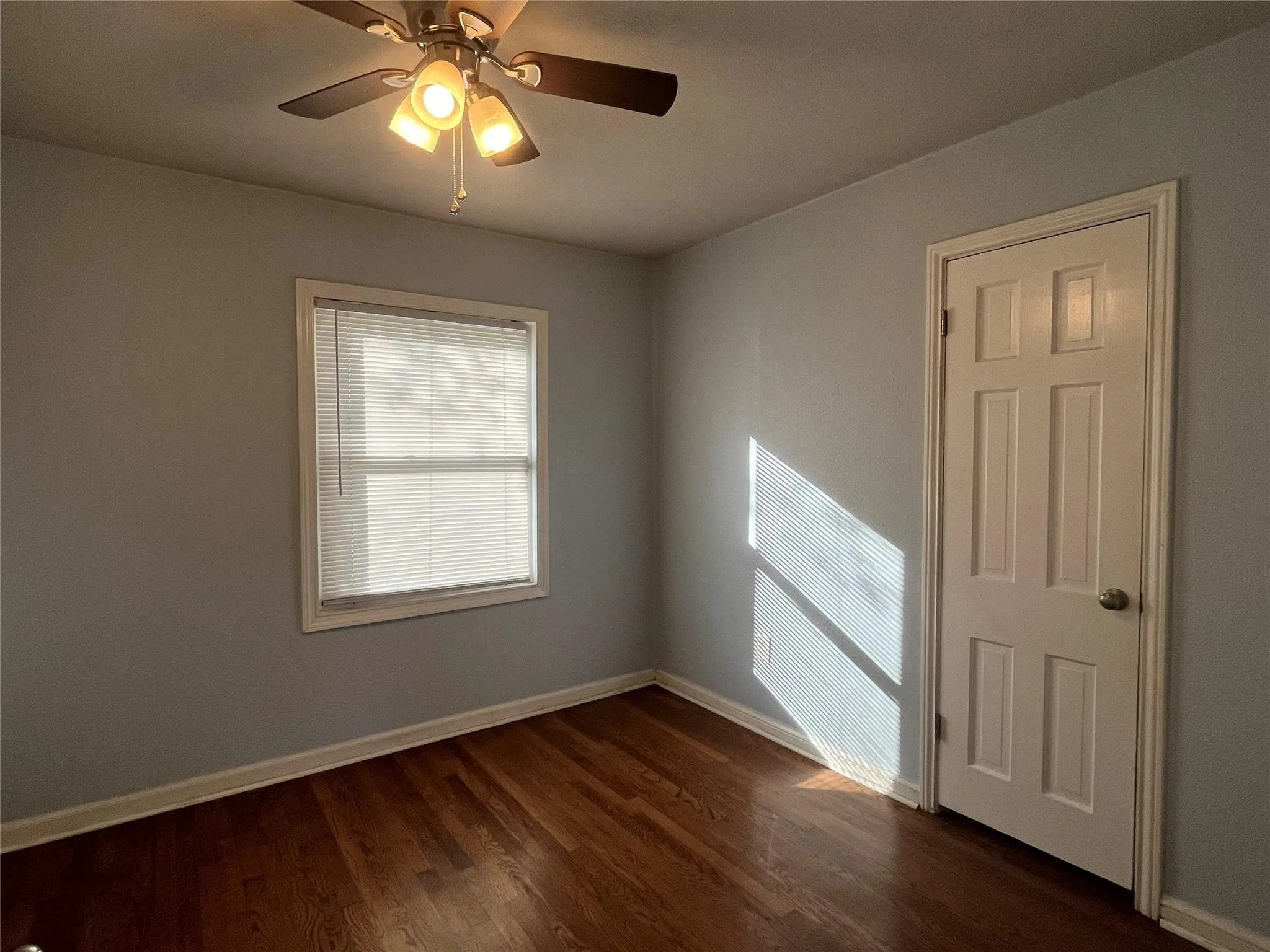 Hardwood flooring, ceiling fan with integrated lighting, paneled door, and window with blinds