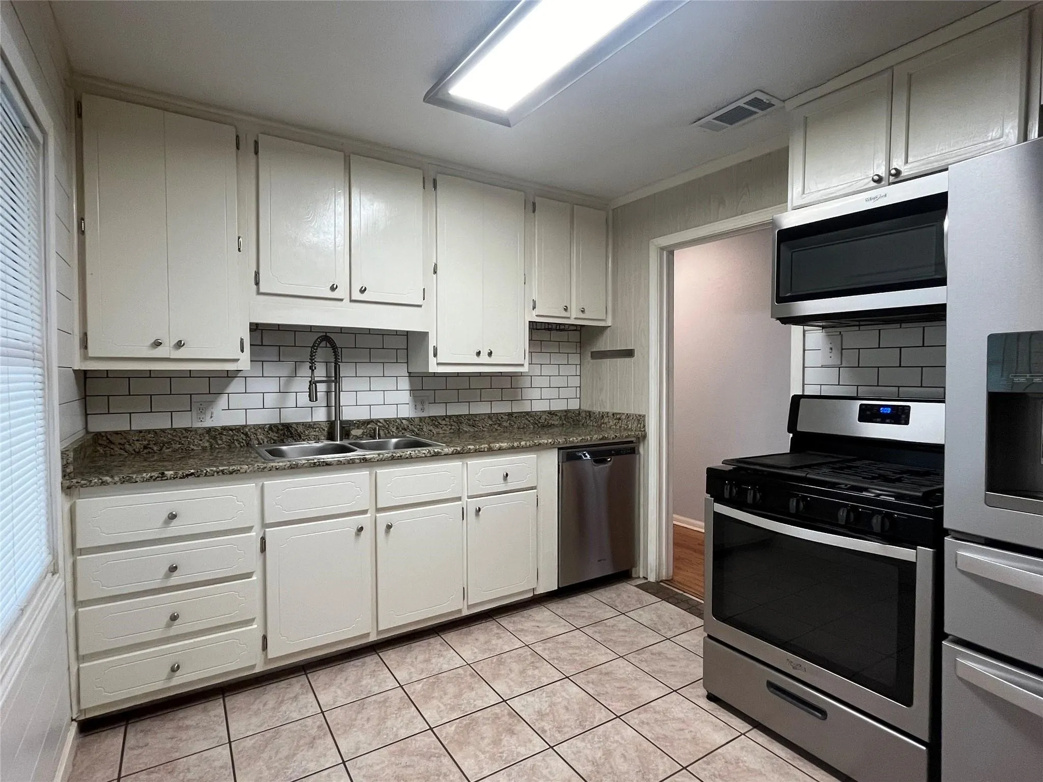 Kitchen featuring white cabinetry, subway tile backsplash, granite-style countertops, stainless steel appliances, and tiled flooring