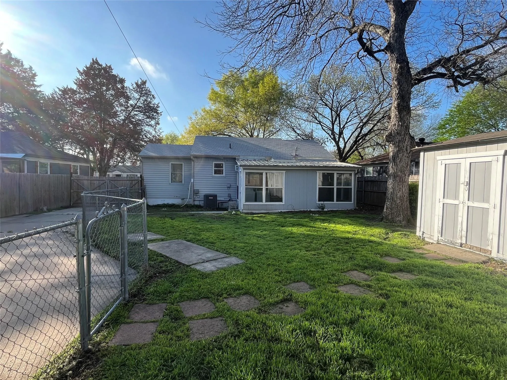 Expansive backyard with a storage shed, established tree, and concrete stepping stones