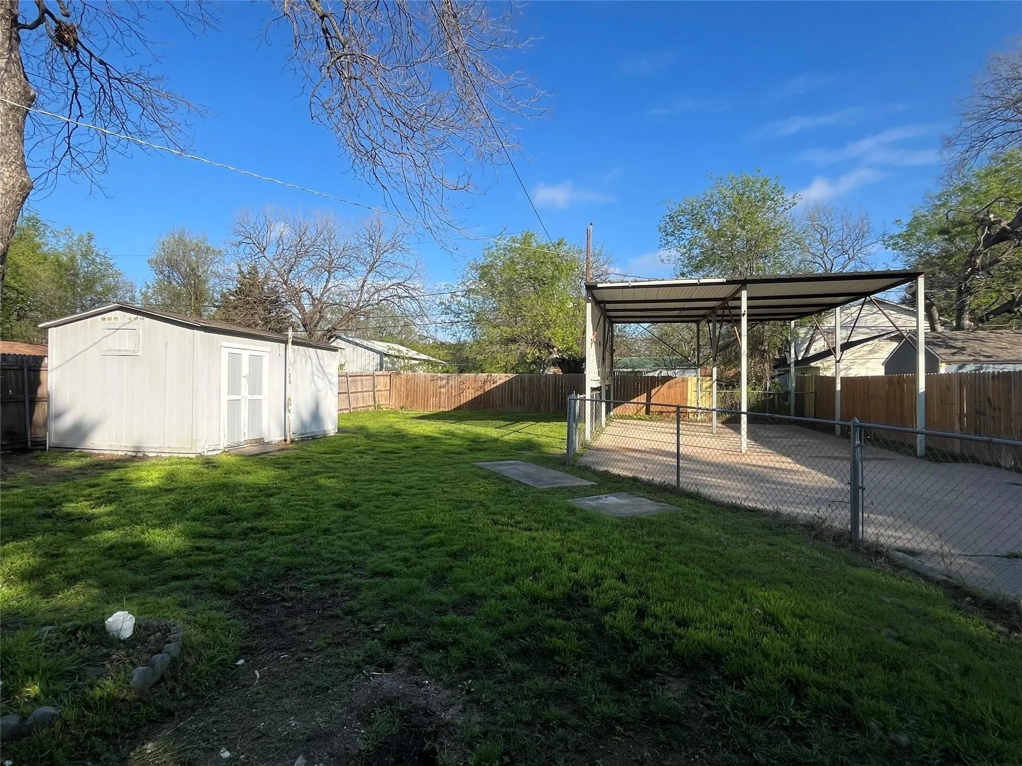 Expansive green space featuring a storage shed, wood fencing, and a covered carport structure