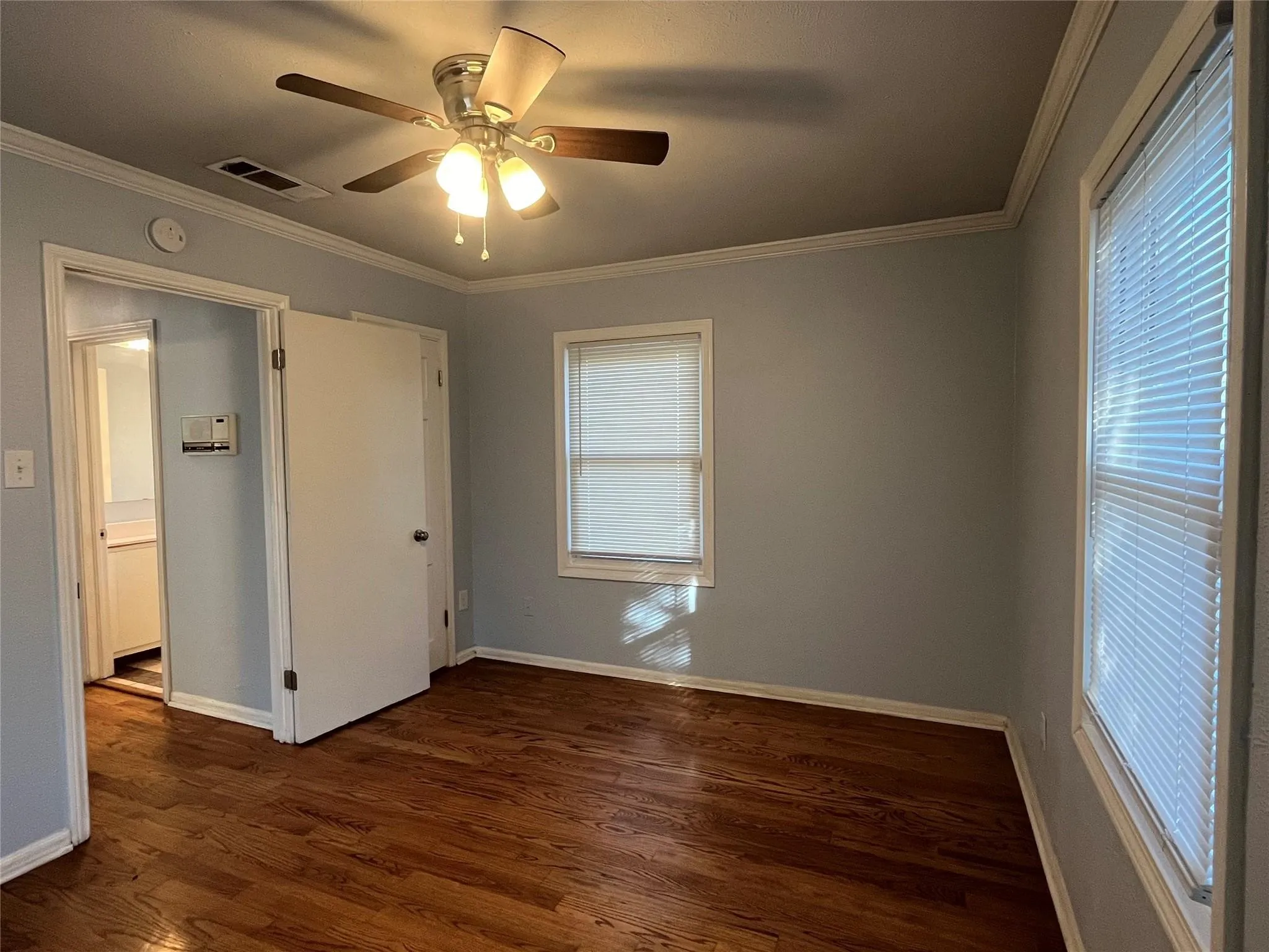 Wood-finish flooring, ceiling fan with integrated lighting, multiple windows with blinds, and painted walls with crown molding