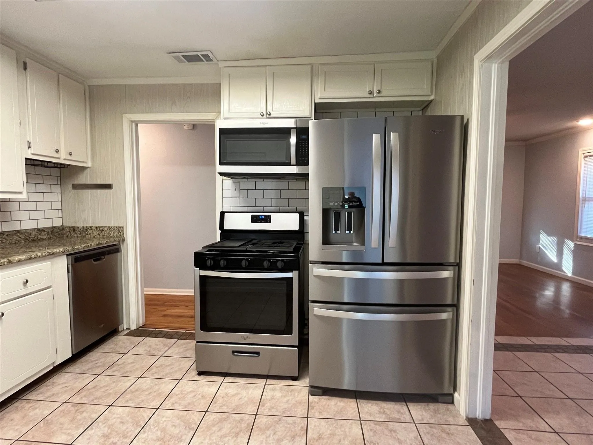 Kitchen featuring white cabinetry, subway tile backsplash, stainless steel appliances, granite-look countertops, and tile flooring
