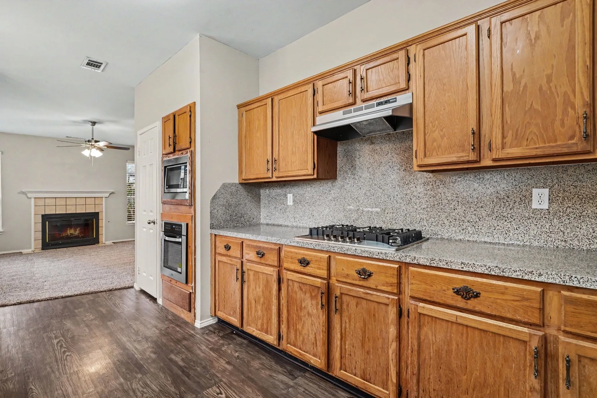 Open floorplan: View of stained kitchen cabinets, gas drop-in gas cooktop, wall oven and microwave opened to the family room.