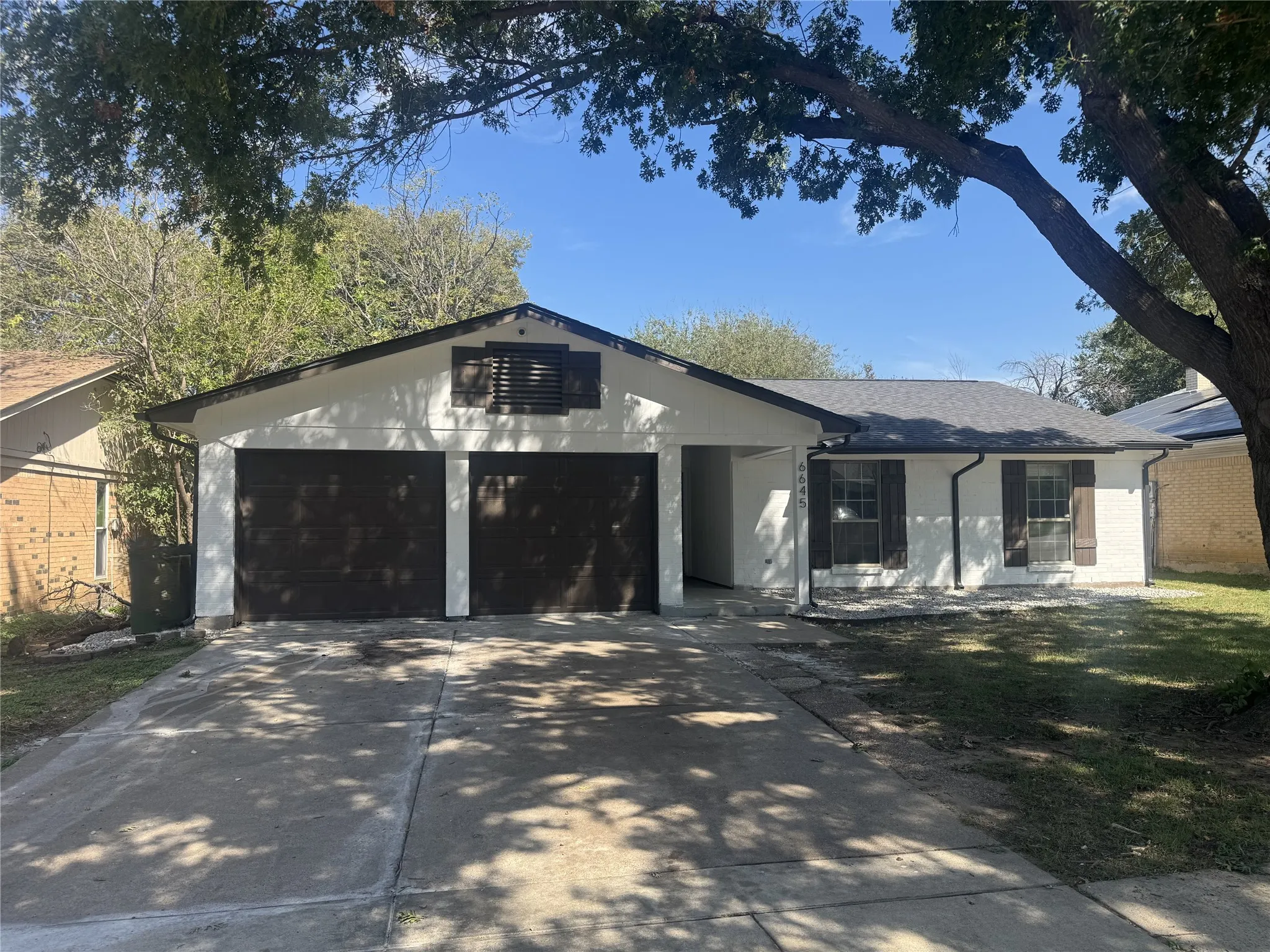White exterior with dark trim and shutters, two-car garage, and a gabled roof