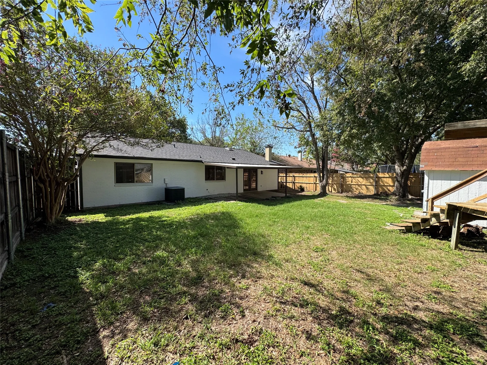 Expansive backyard featuring a manicured lawn, established trees, and a wooden privacy fence