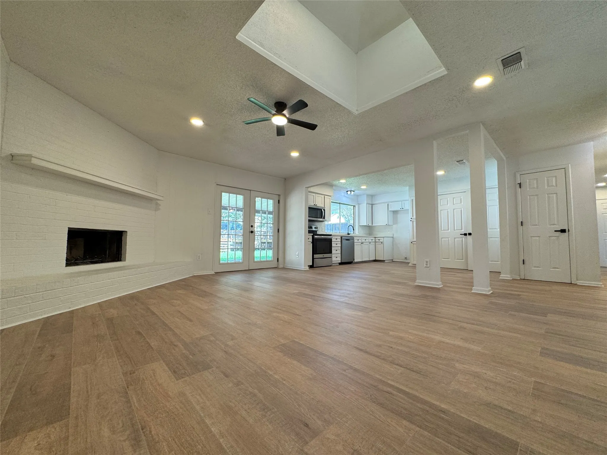 Spacious living area featuring wood-finish flooring, a white brick fireplace, and dual French doors