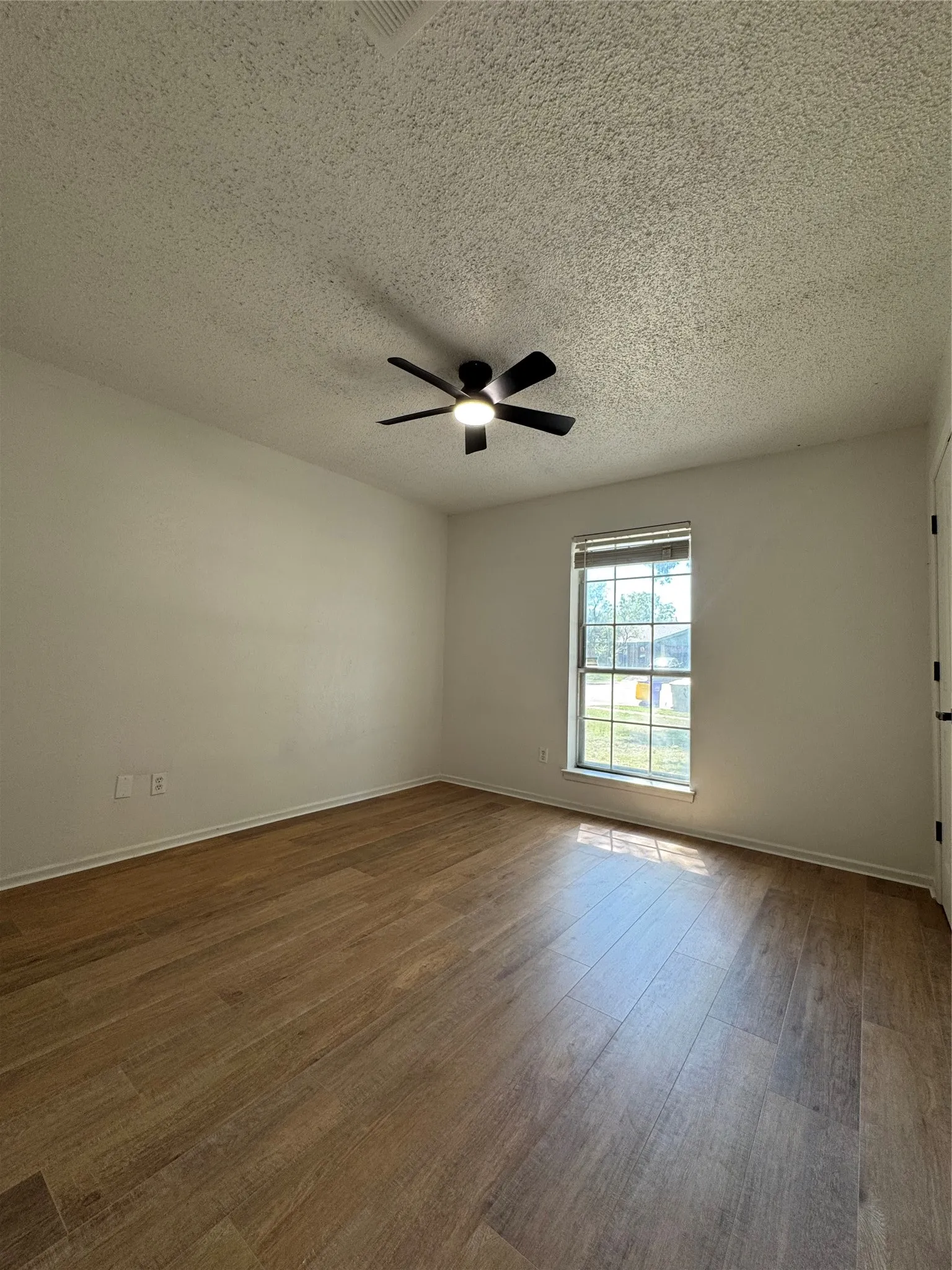 Wood-finish flooring with a satin finish, single window with blinds, and a ceiling fan with integrated lighting