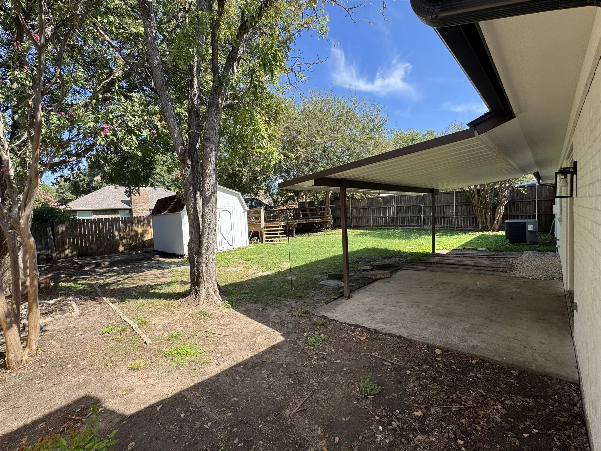 Expansive backyard with a covered patio, concrete pad, storage shed, and mature trees