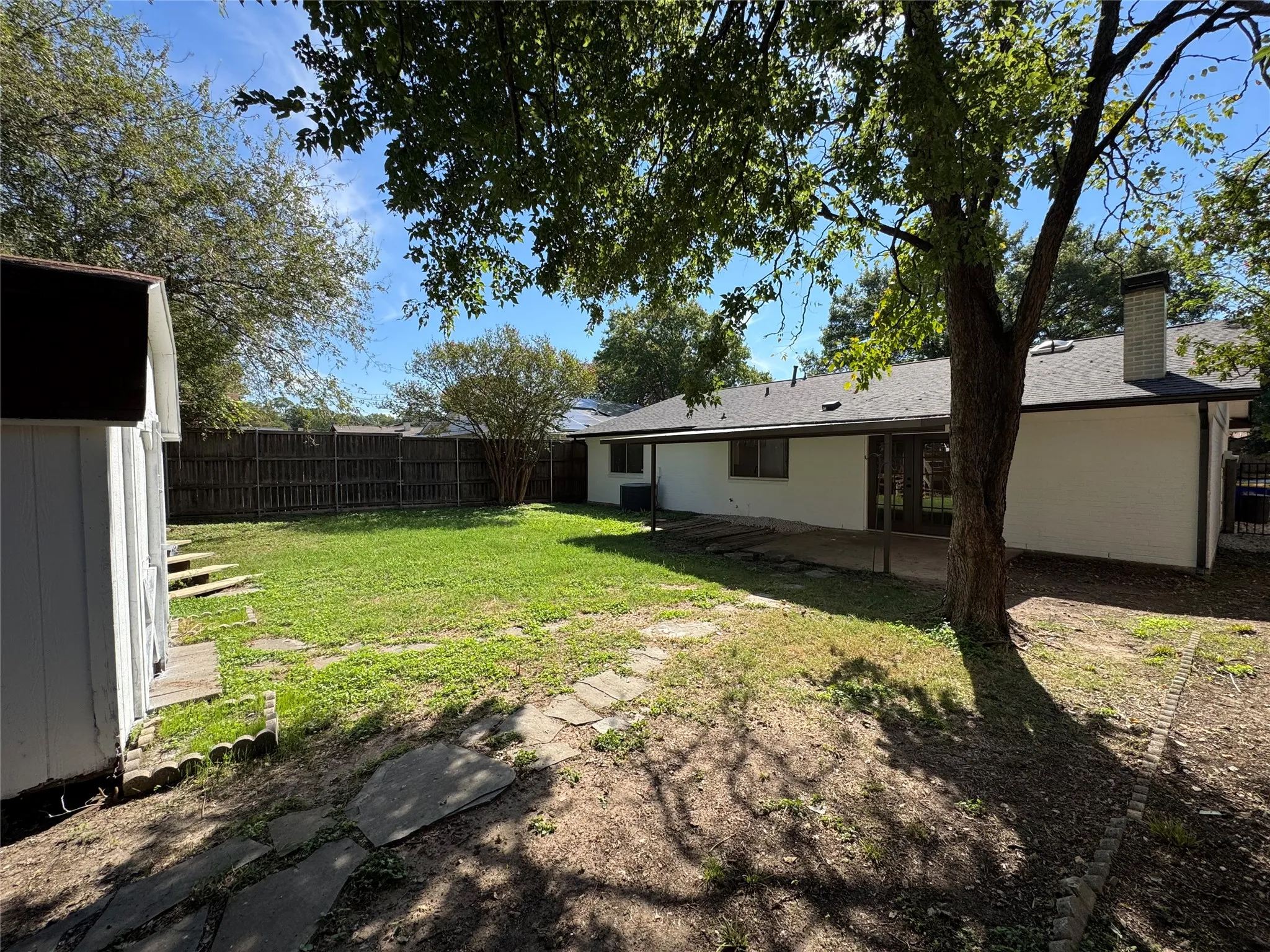 Expansive backyard with a manicured lawn, full privacy fencing, established shade trees, and a detached storage shed
