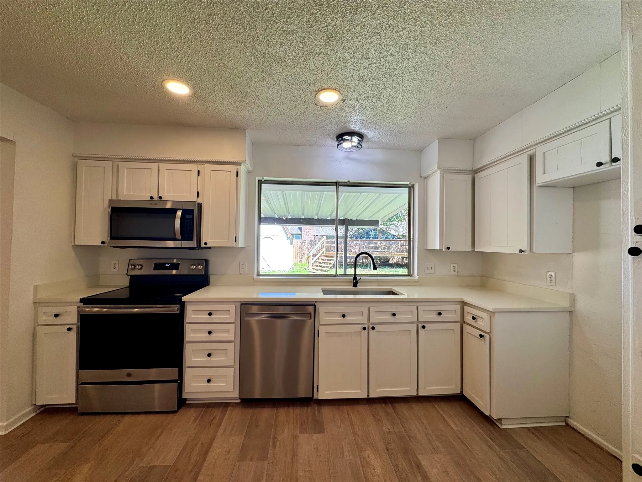 Kitchen featuring wood-finish flooring, white cabinetry, integrated stainless steel appliances, light-toned countertops, and an undermount sink with a gooseneck faucet