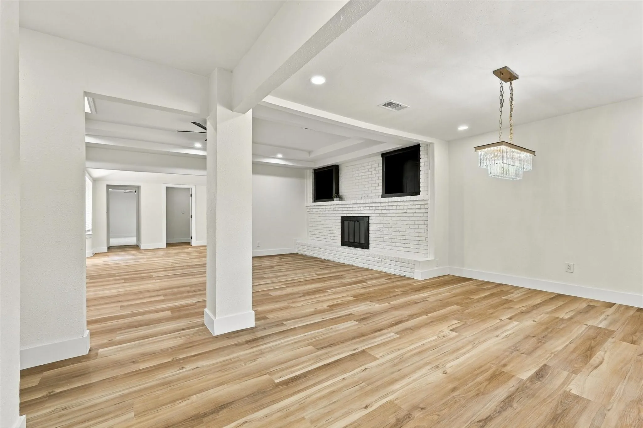 Spacious living area featuring wood-finish flooring, a white brick fireplace with a black grate, a ceiling fan, and recessed lighting