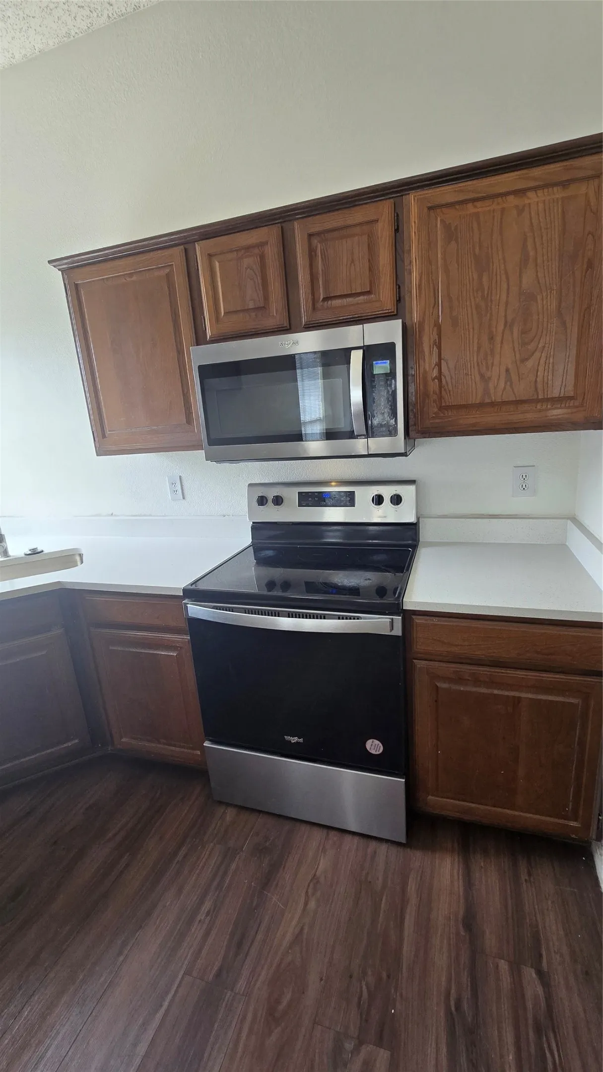 Hardwood-finish flooring, white countertops, built-in wooden cabinetry, stainless steel microwave, and a stainless steel oven range