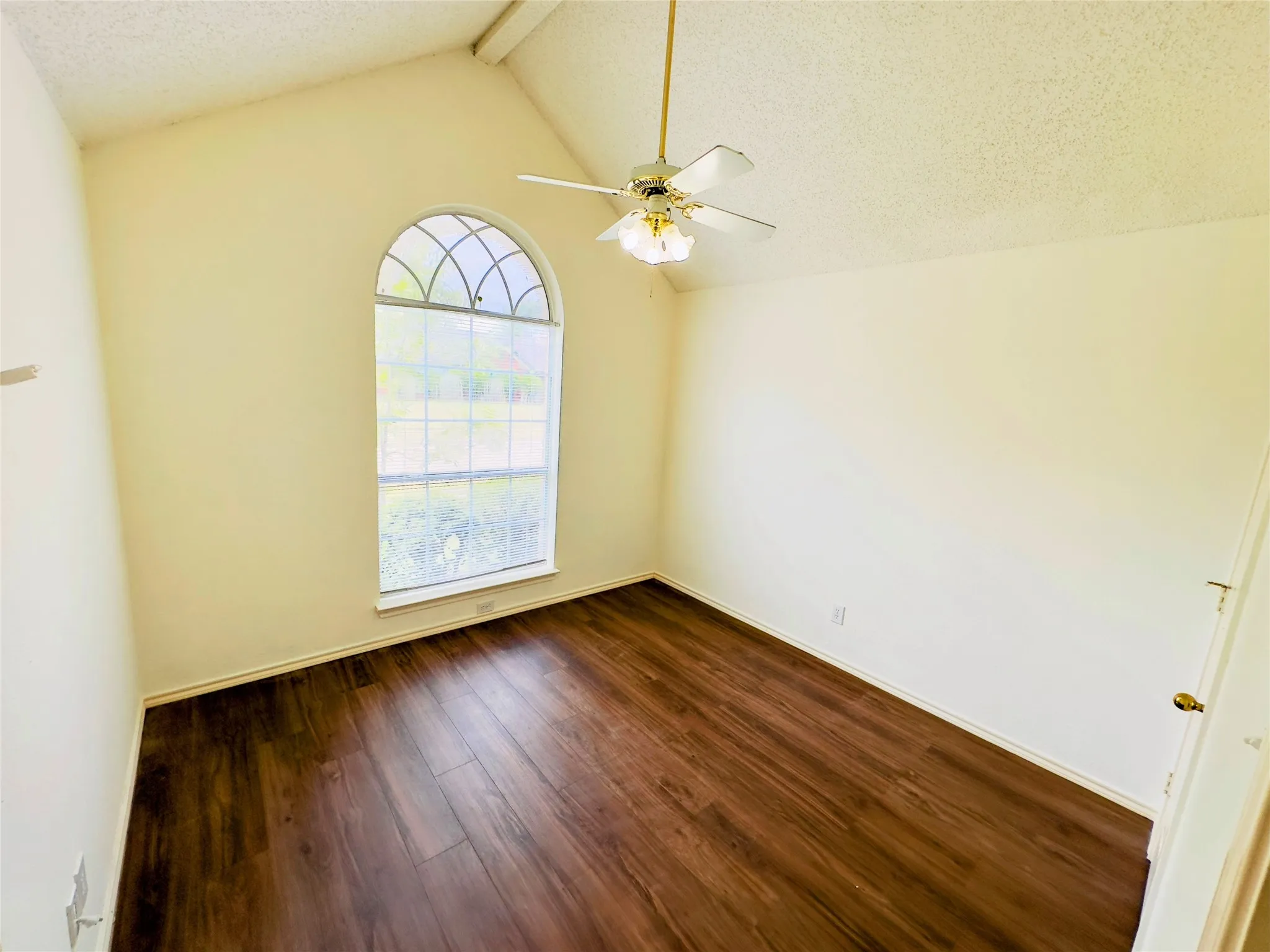 Vaulted ceiling with a ceiling fan, arched window, and wood-finish flooring