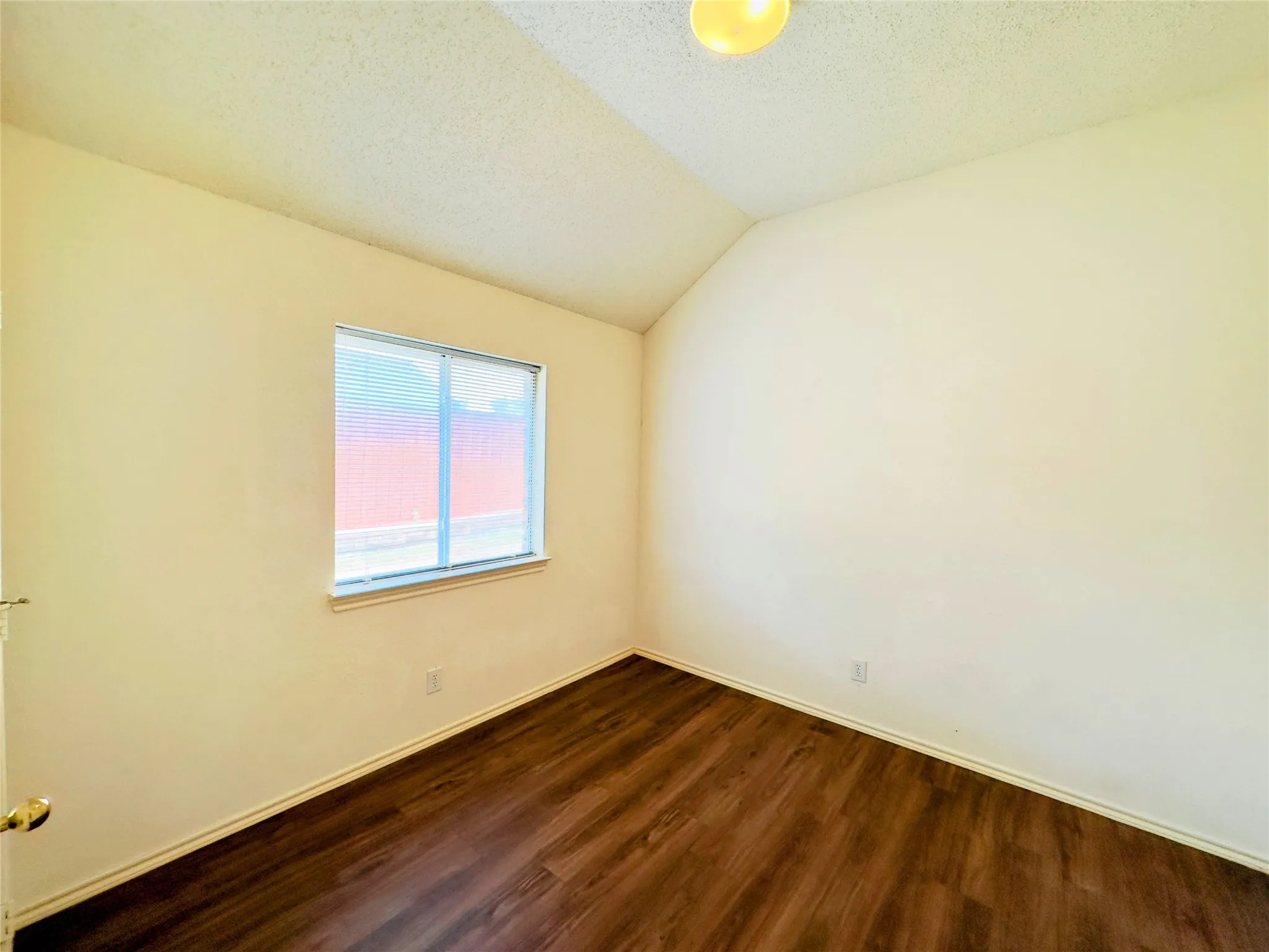 Bright bedroom featuring warm yellow walls, wood-finish flooring, and a large window with natural light exposure