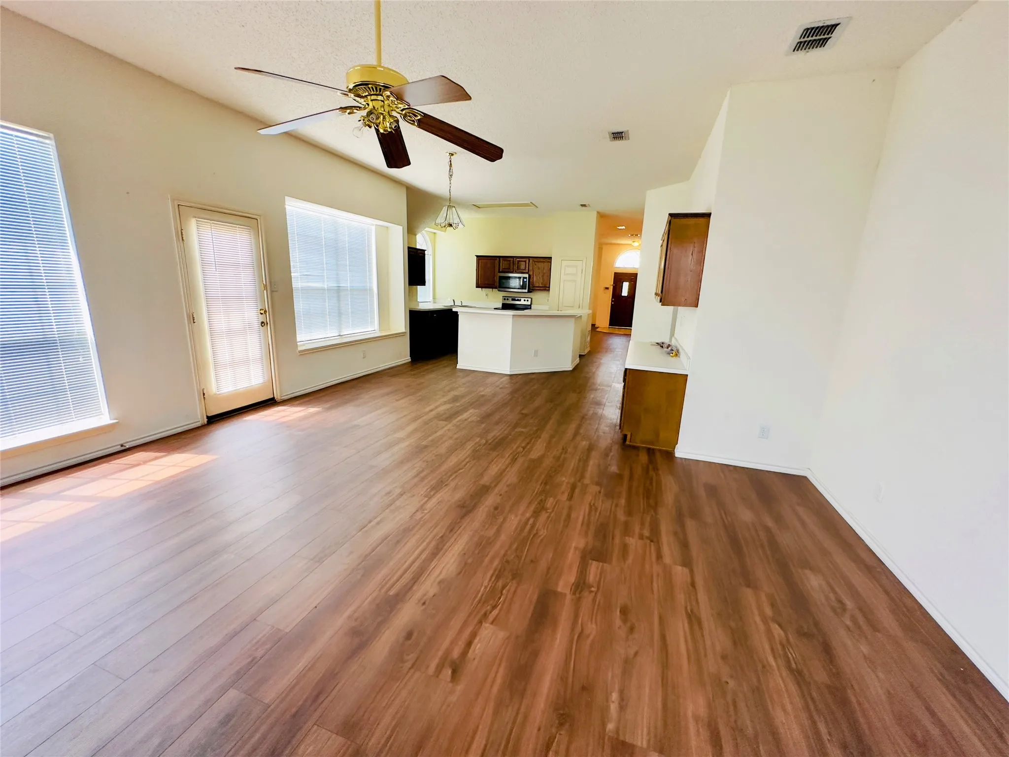 Spacious interior with wood-finish flooring, a ceiling fan, and multiple windows