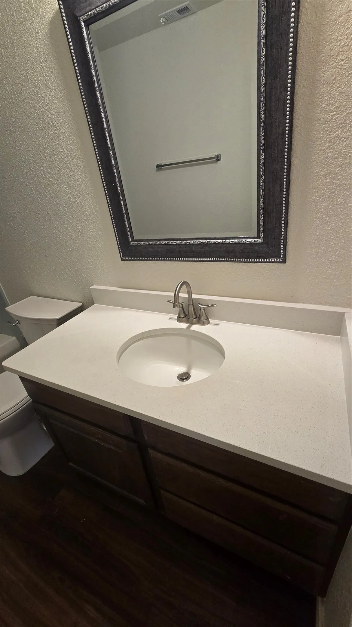 Dark wood-finish vanity with an integrated sink, light-toned countertop, and framed mirror