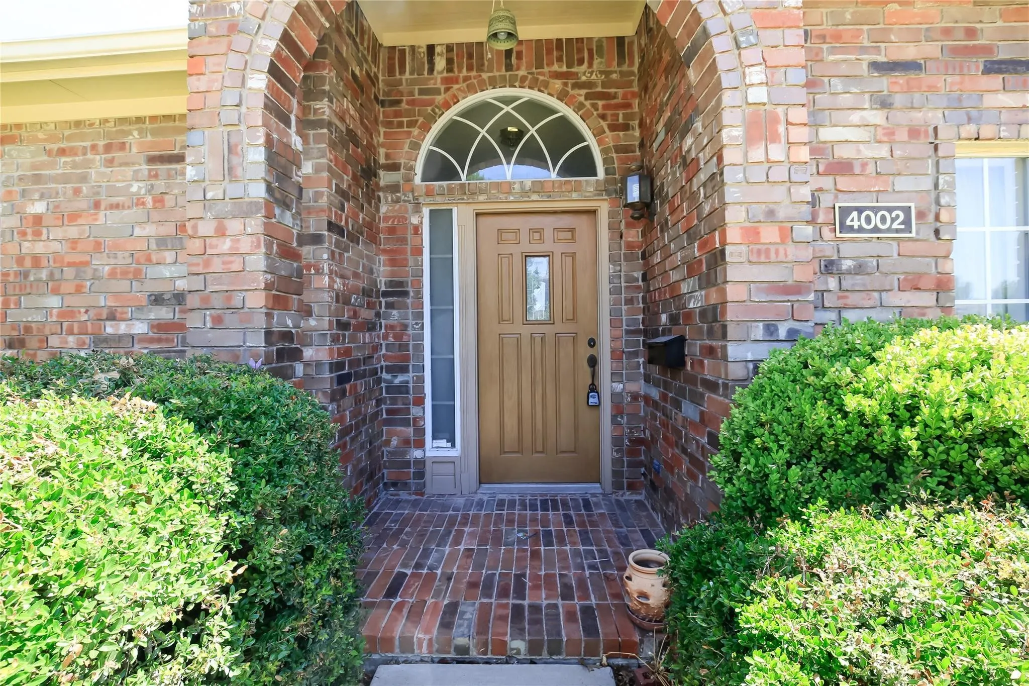 Brick facade with an arched entry, a light wood-finish door, and a decorative transom window