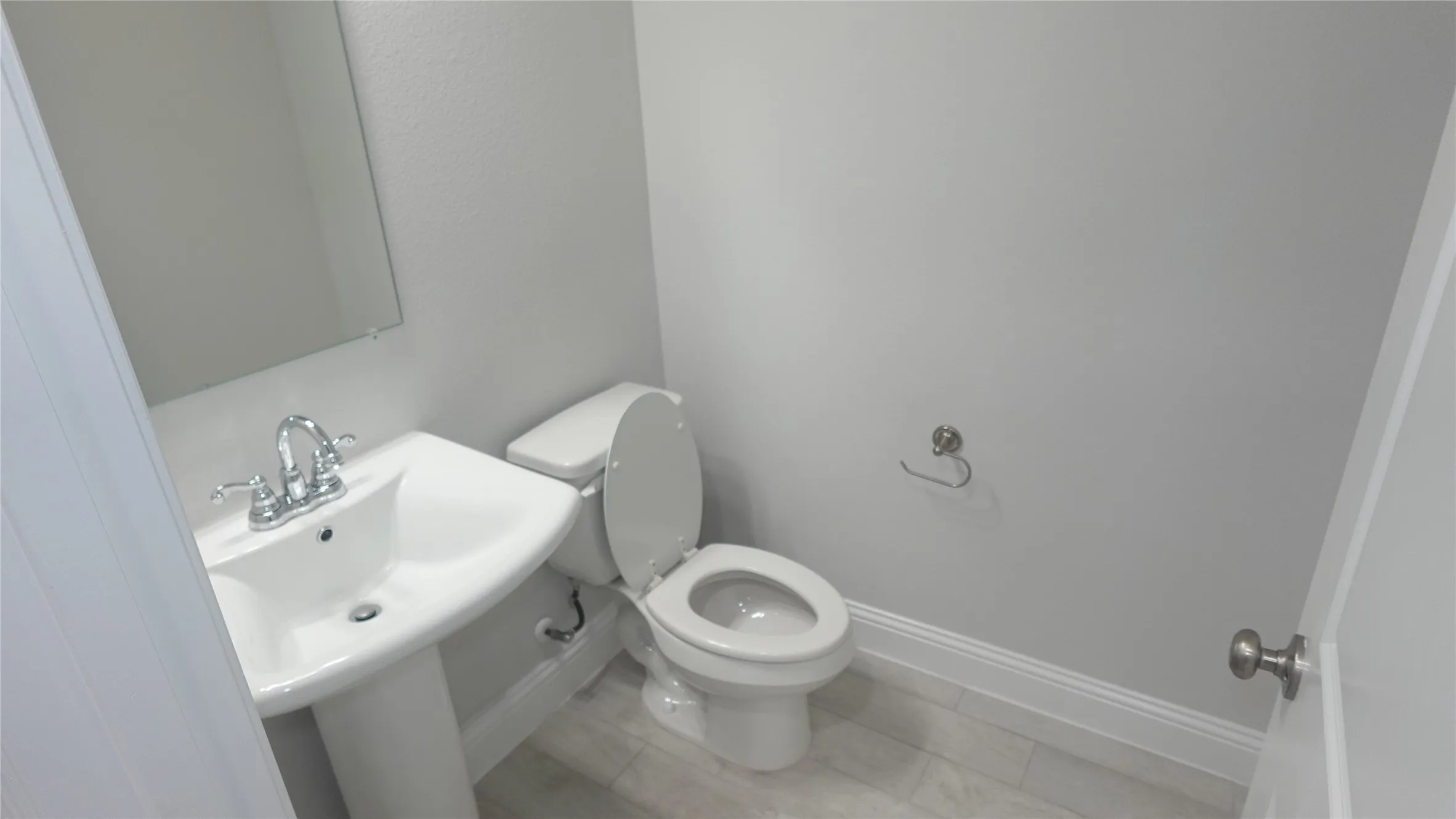 Pedestal sink with chrome faucet, wall-mounted mirror, ceramic tile flooring, and a white commode