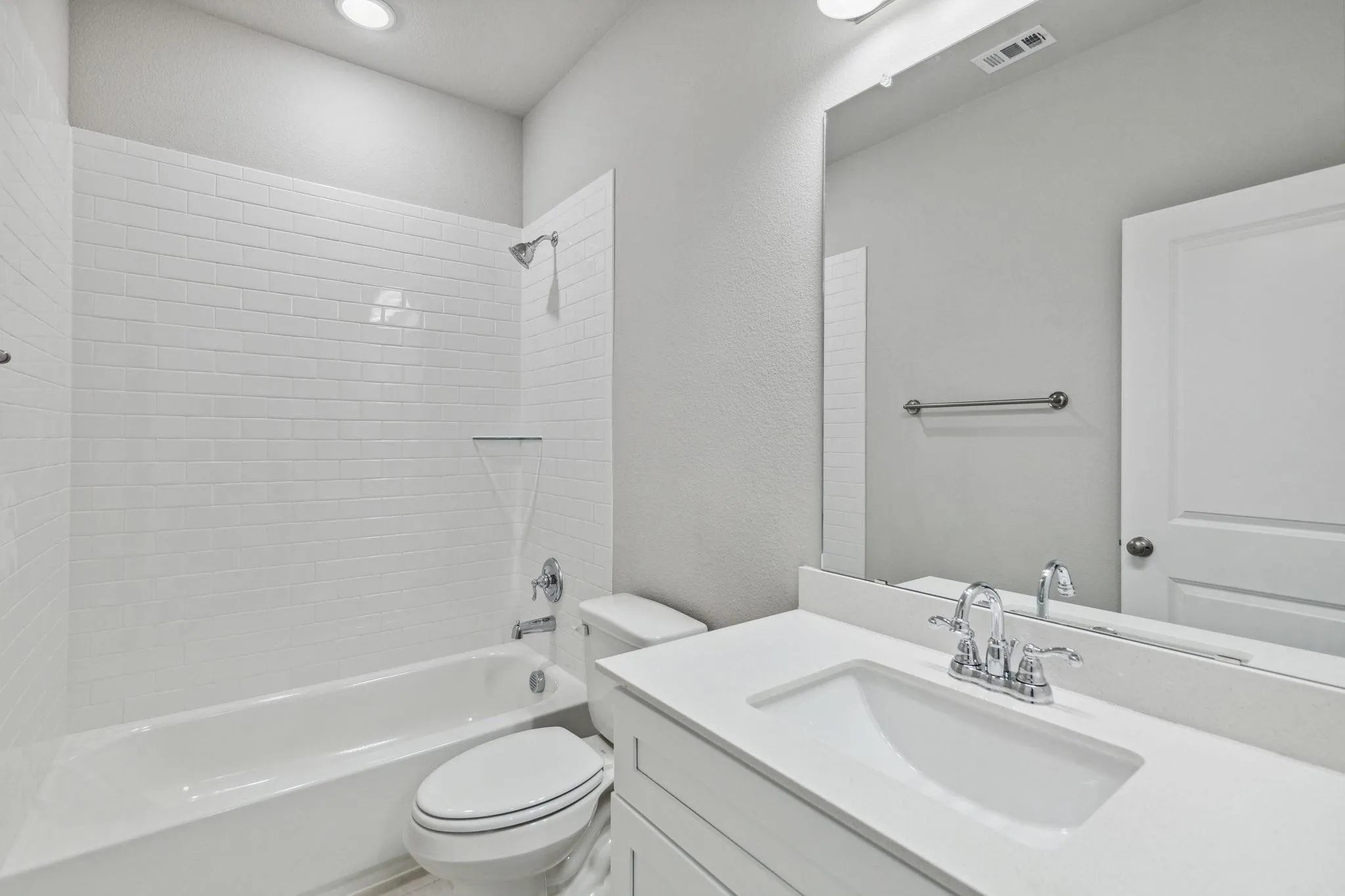Bathroom featuring a white subway tile shower surround, a built-in tub, a white vanity with an integrated sink, a large wall-mounted mirror, and overhead lighting