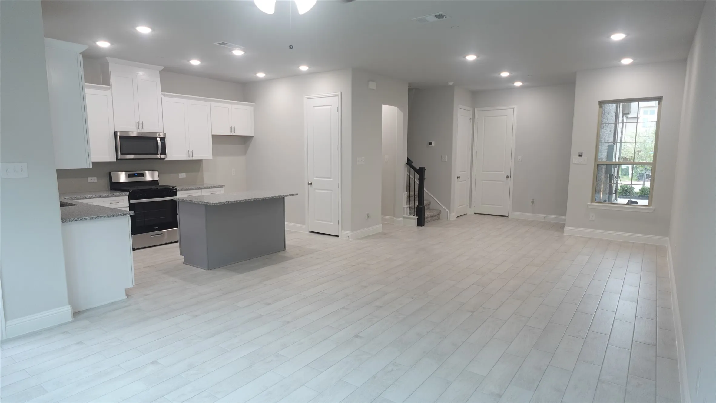 Open-concept living space with light wood-finish flooring, recessed lighting, and a kitchen featuring white cabinetry, stainless steel appliances, and a central island