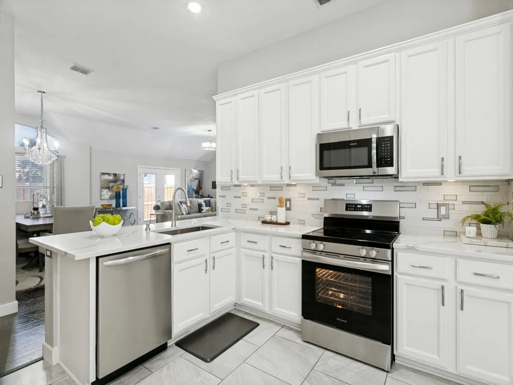 White cabinetry with stainless steel hardware, undermount kitchen sink, stainless steel appliances, patterned tile backsplash, and light-toned tile flooring
