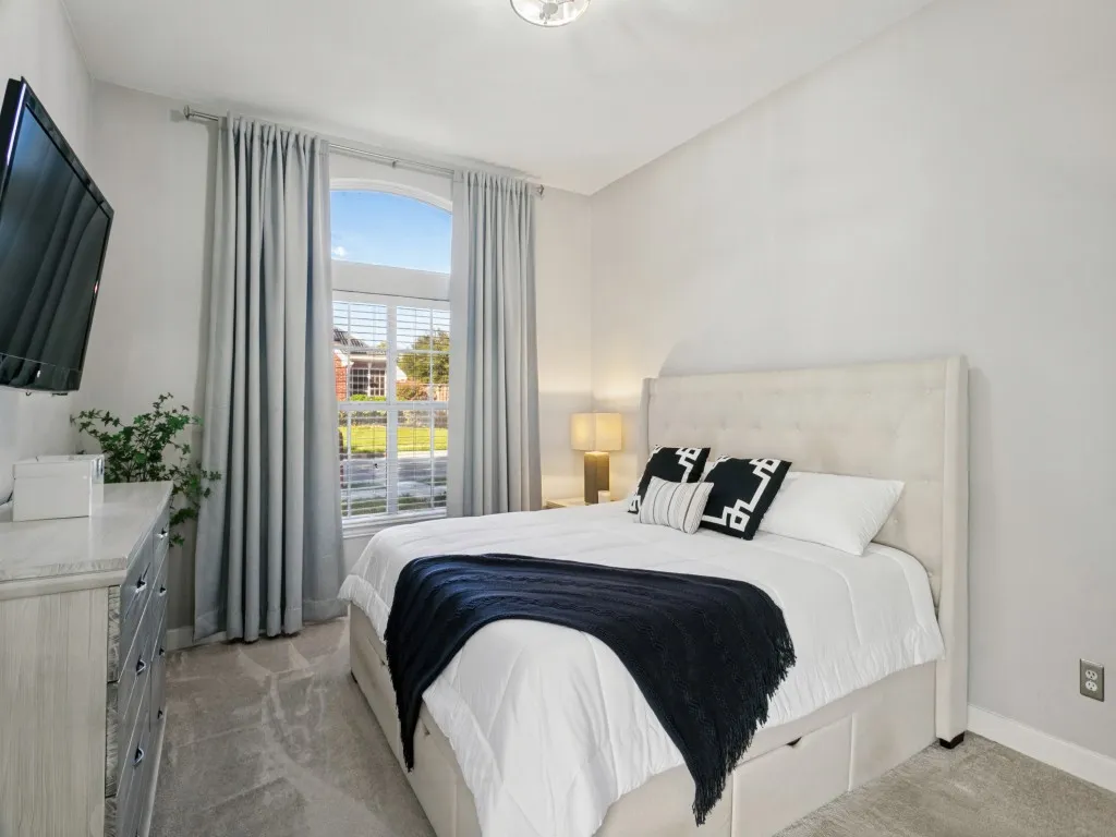 Arch-top window, wall-mounted television, recessed lighting fixture, light-toned wall paint, and gray carpet