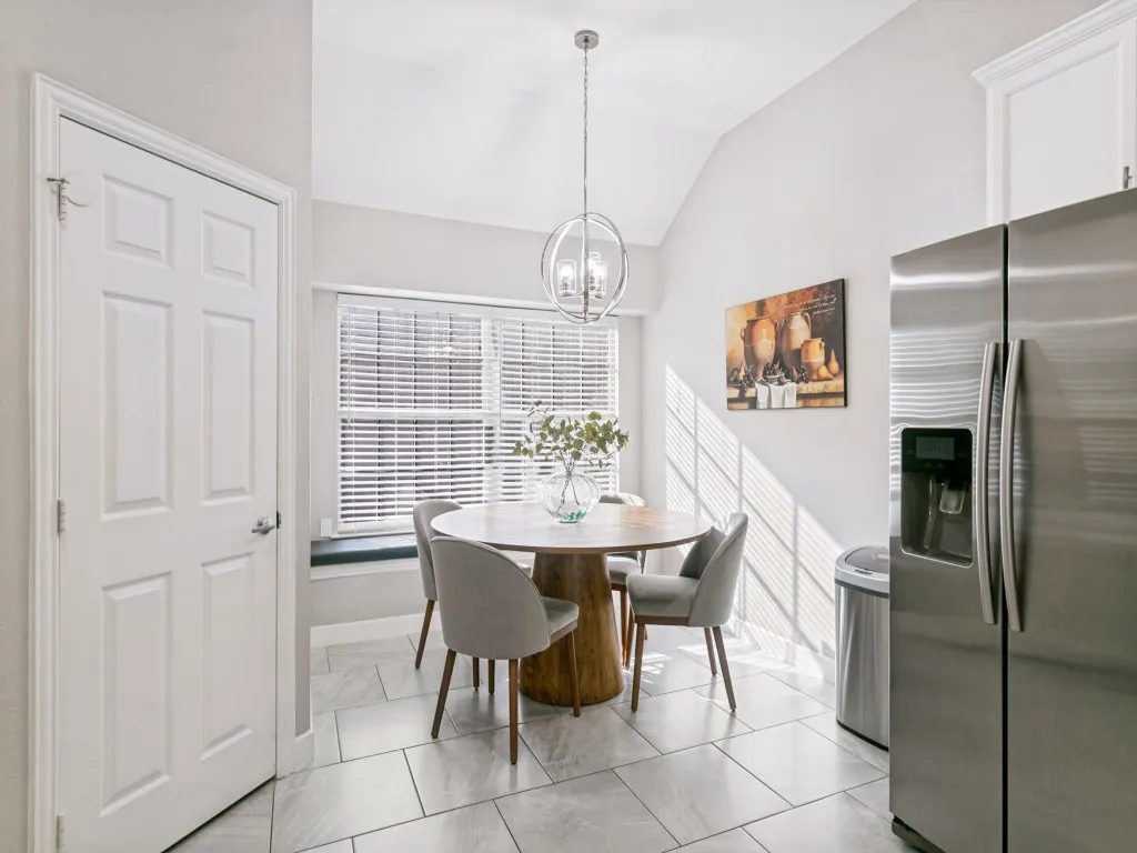 Vaulted ceiling with a contemporary chandelier, large window with blinds, stainless steel refrigerator, and light-toned tile flooring