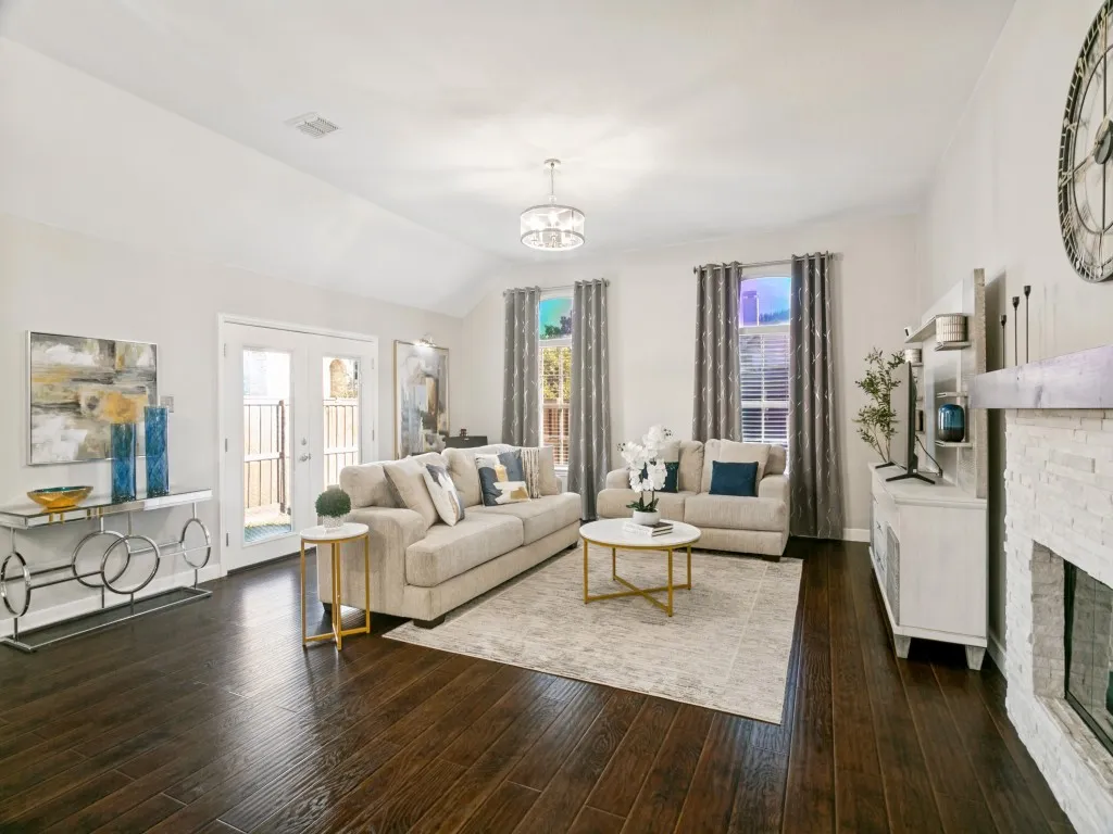Vaulted ceiling with a chandelier, dark wood-finish flooring, double French doors, and a stone-clad fireplace