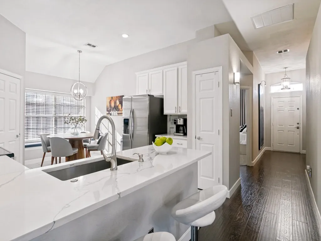 Kitchen with white cabinetry, stainless steel appliances, and a central island featuring a sink and white stone countertop