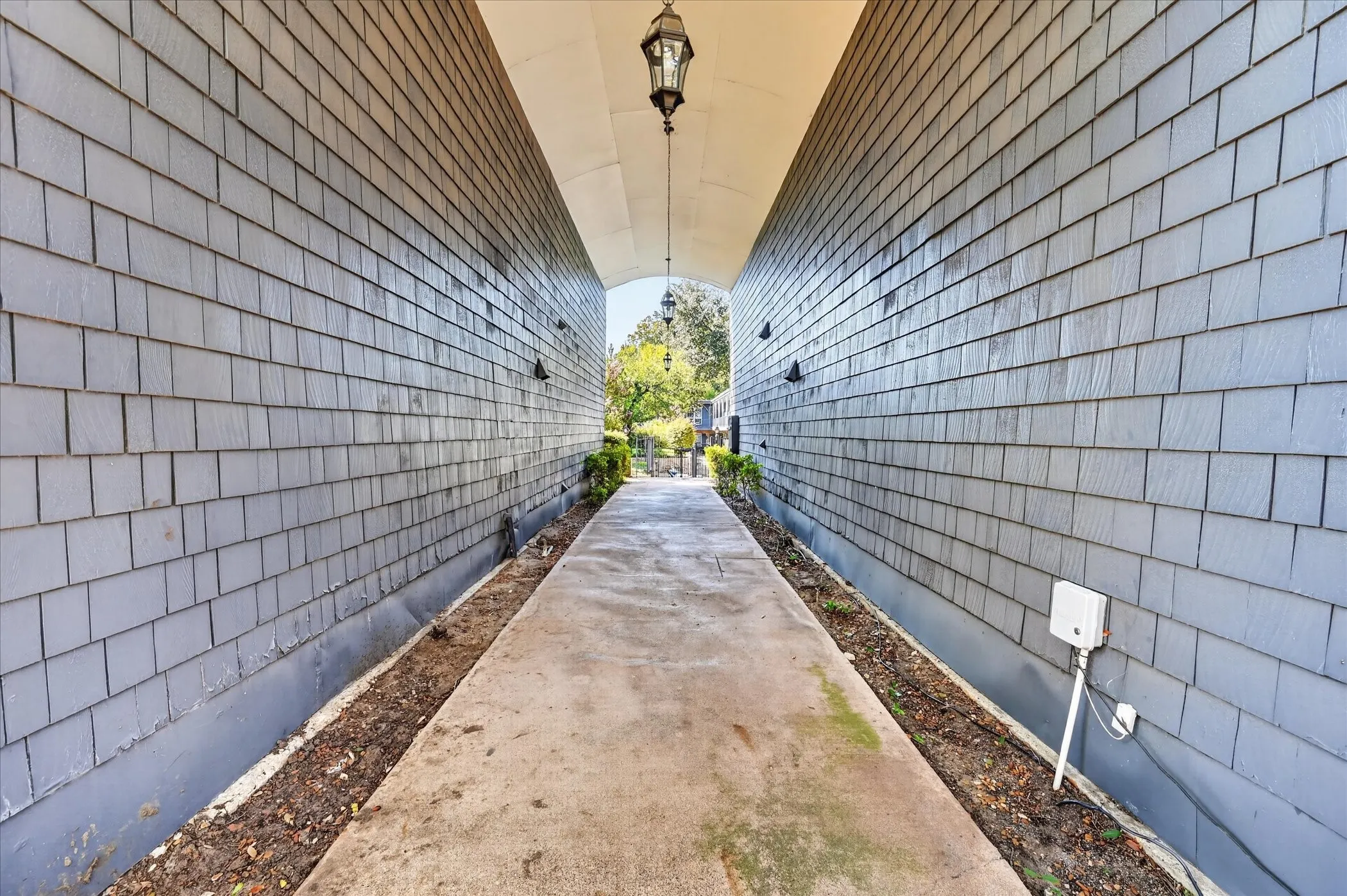 Covered walkway with shake siding, overhead lantern light fixture, and concrete pathway