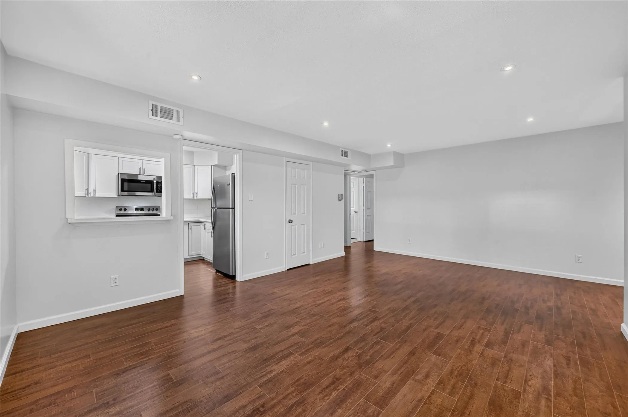 Open-concept living space featuring gleaming vinyl plank wood like finish flooring throughout, recessed ceiling lighting, and white painted interior doors
