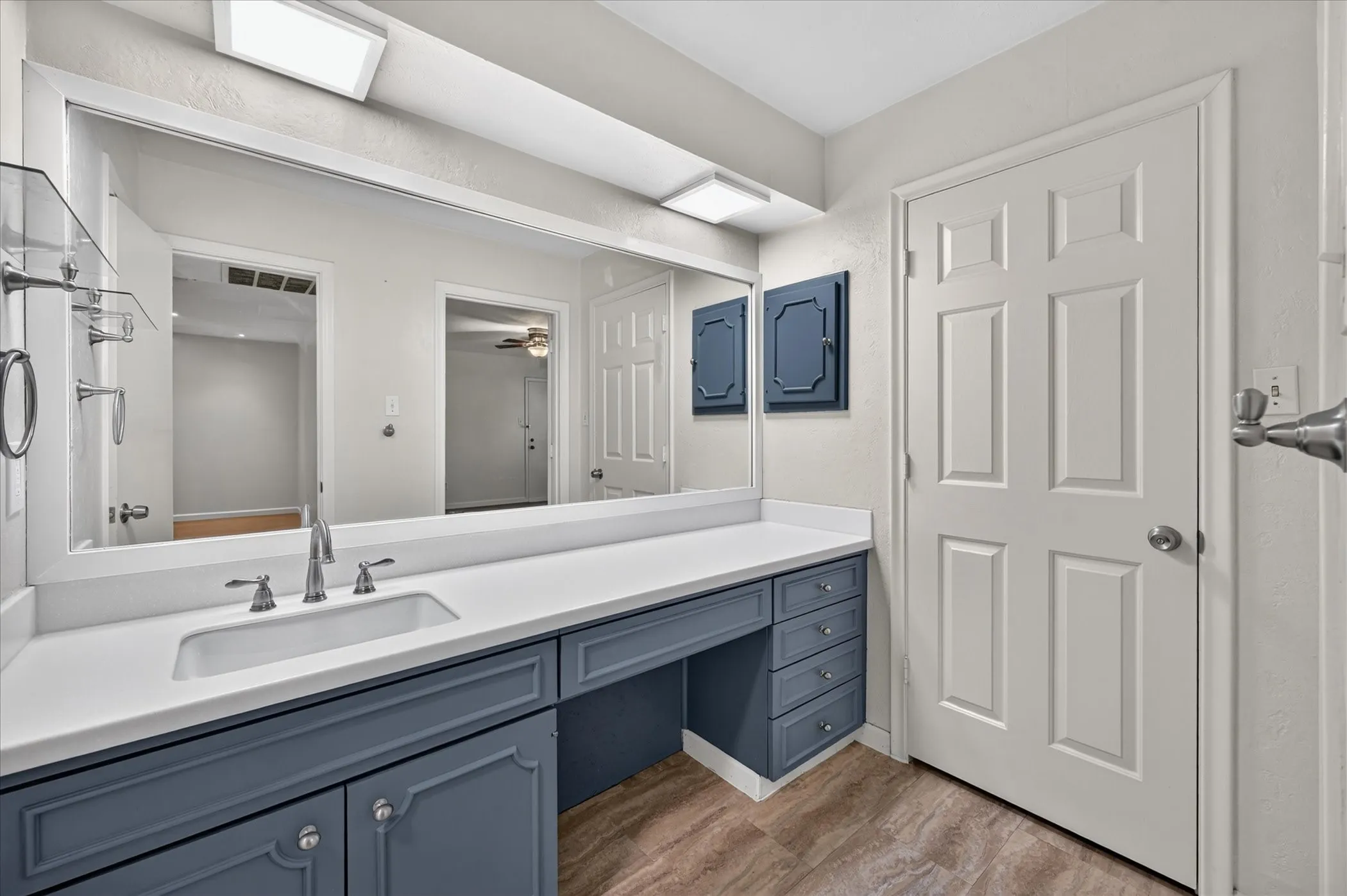 Vanity with integrated sink, expansive counter space, vinyl tile flooring, and a large wall-mounted mirror