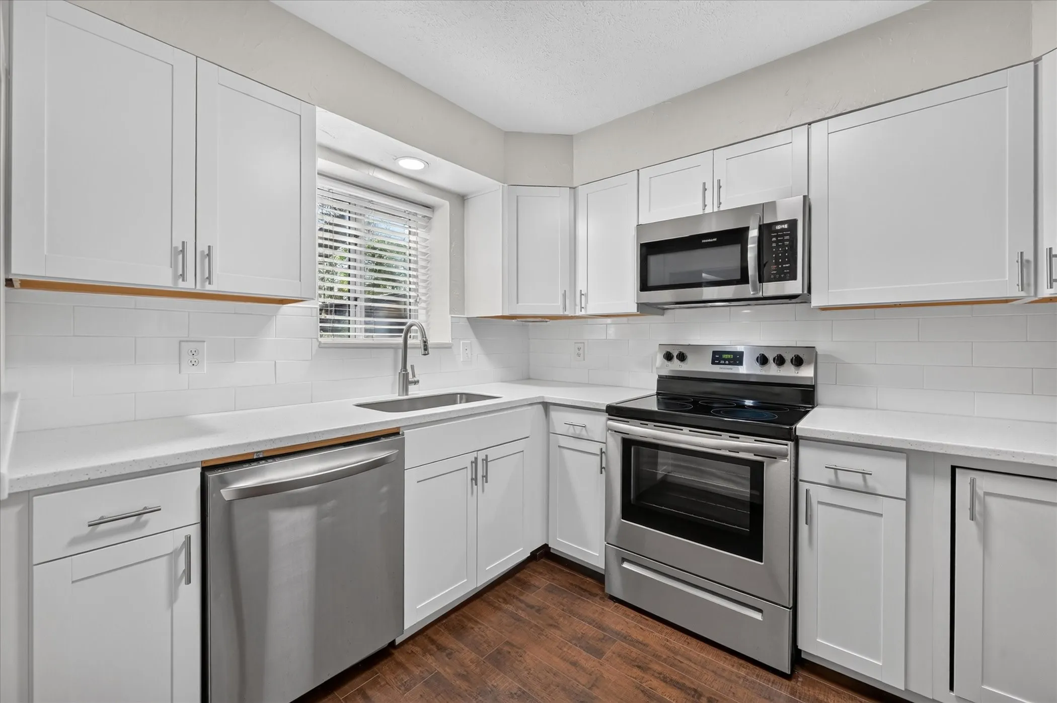 Kitchen featuring white shaker-style cabinetry, stainless steel appliances, white subway tile backsplash, and vinyl plank wood like -finish flooring