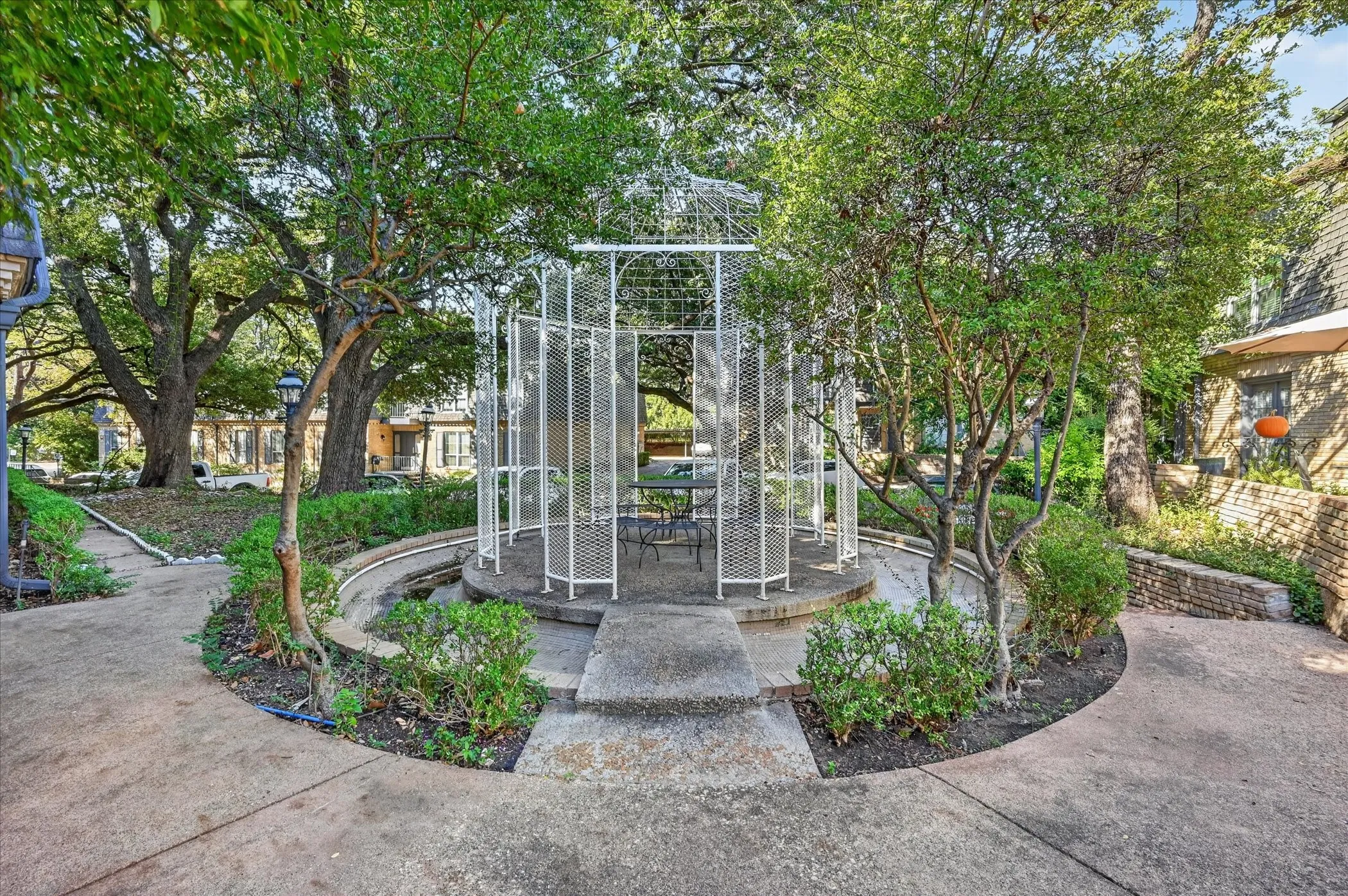 Paved pathway with mature trees, a metal gazebo, and surrounding landscaping
