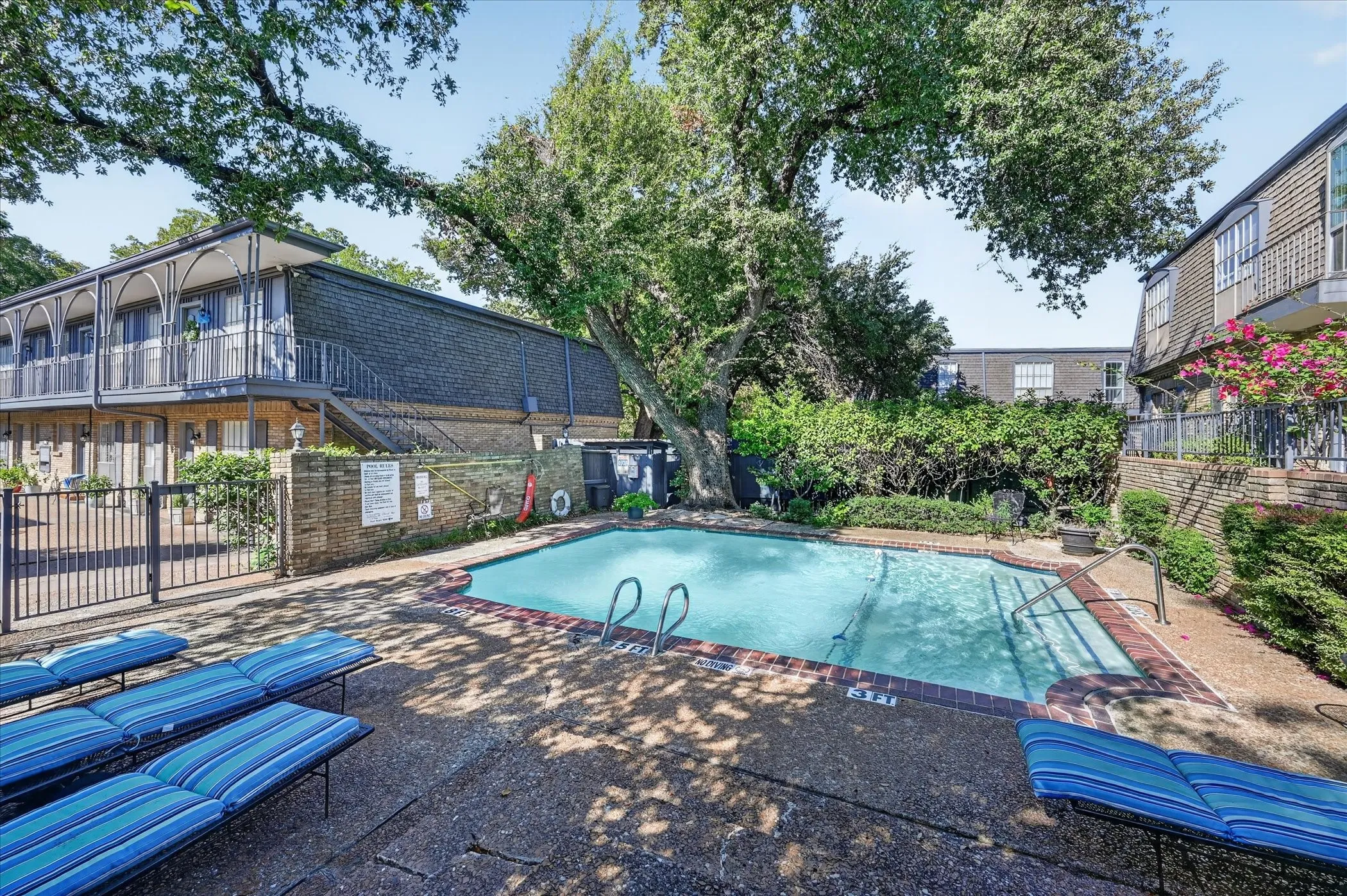 Swimming pool with brick coping, surrounded by mature trees and landscaping