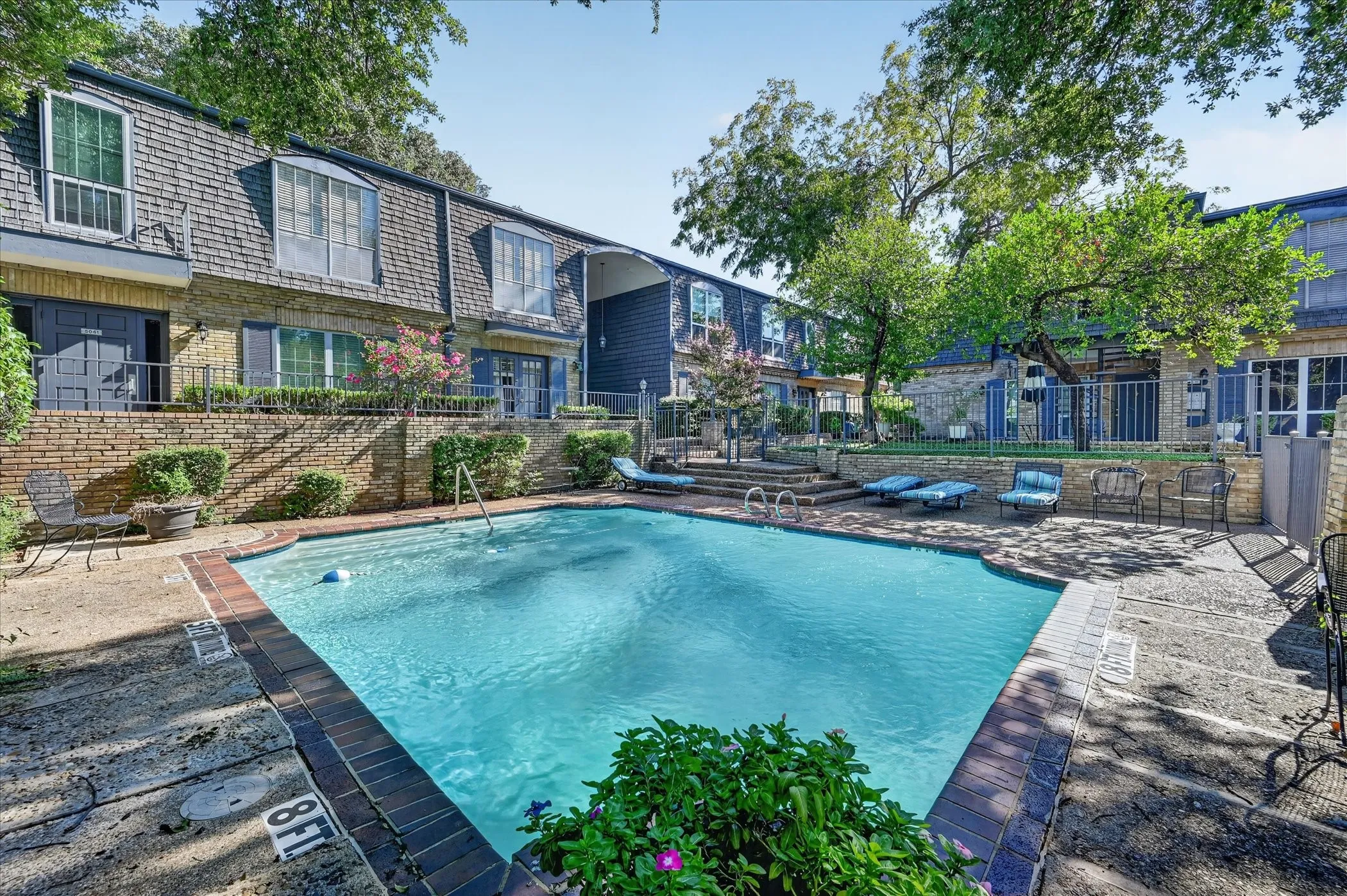 Community swimming pool with water features, surrounded by mature trees
