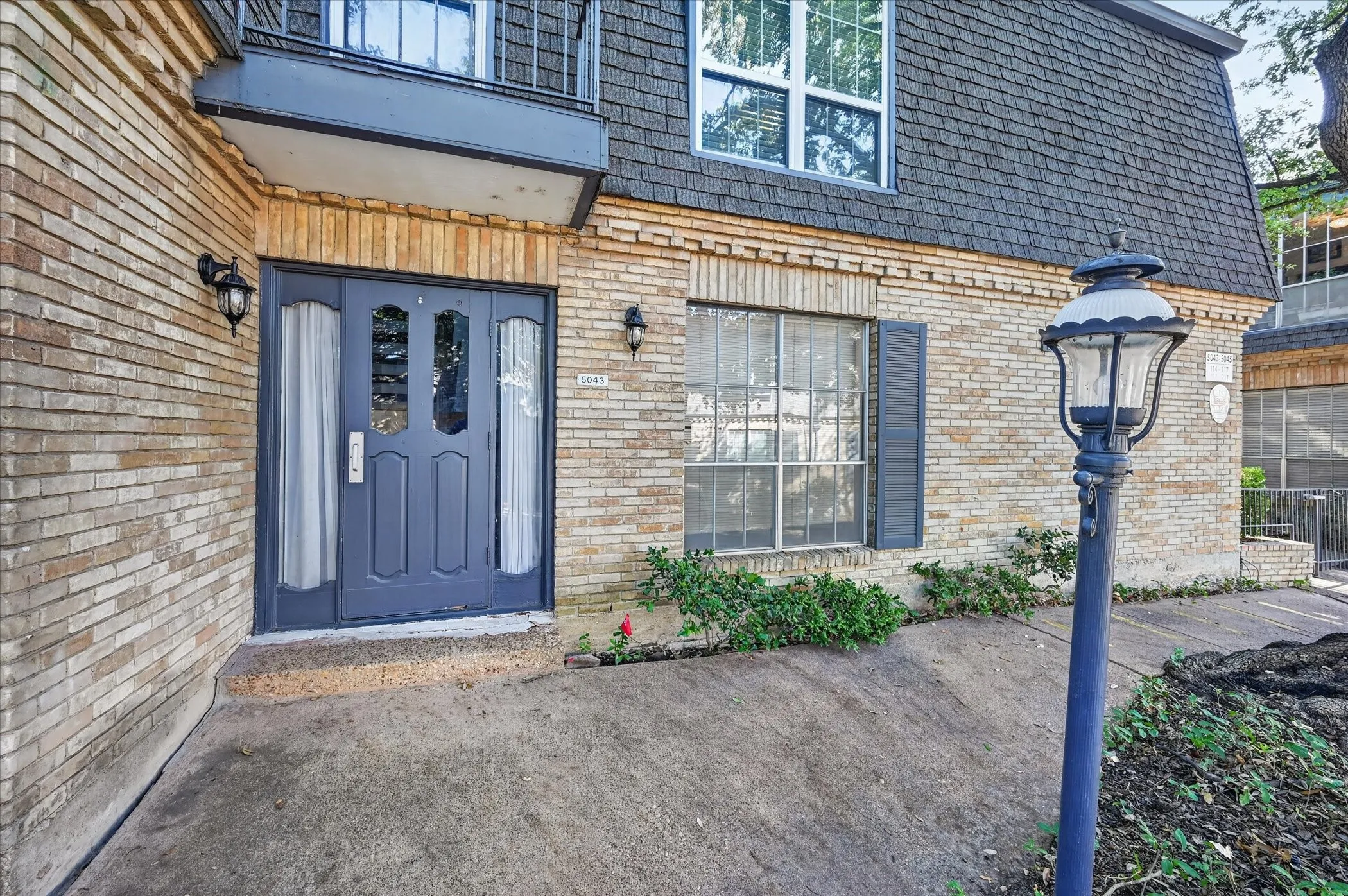Condo entry through the parking area. Brick exterior with a dark-paneled entry door, adjacent sidelights, and exterior wall sconces