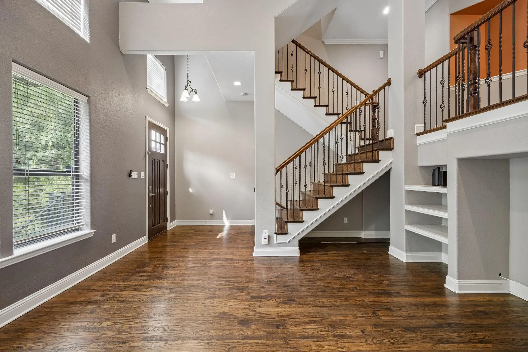Hardwood-finish flooring, a grand staircase with wrought iron balusters, a dark wood-paneled entry door, and built-in shelving