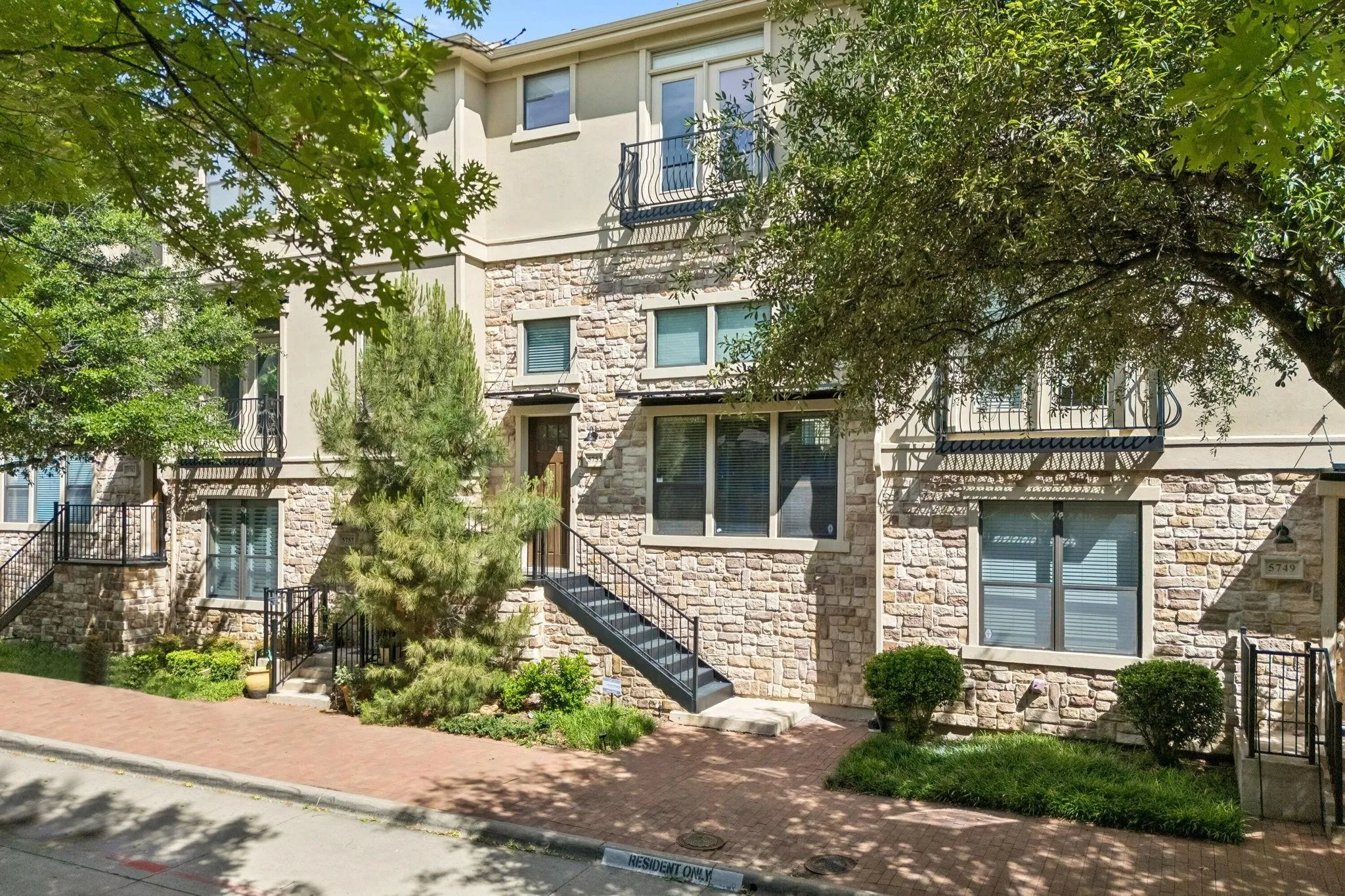 Stone and stucco facade with black metal railings, front entry staircase, and mature landscaping