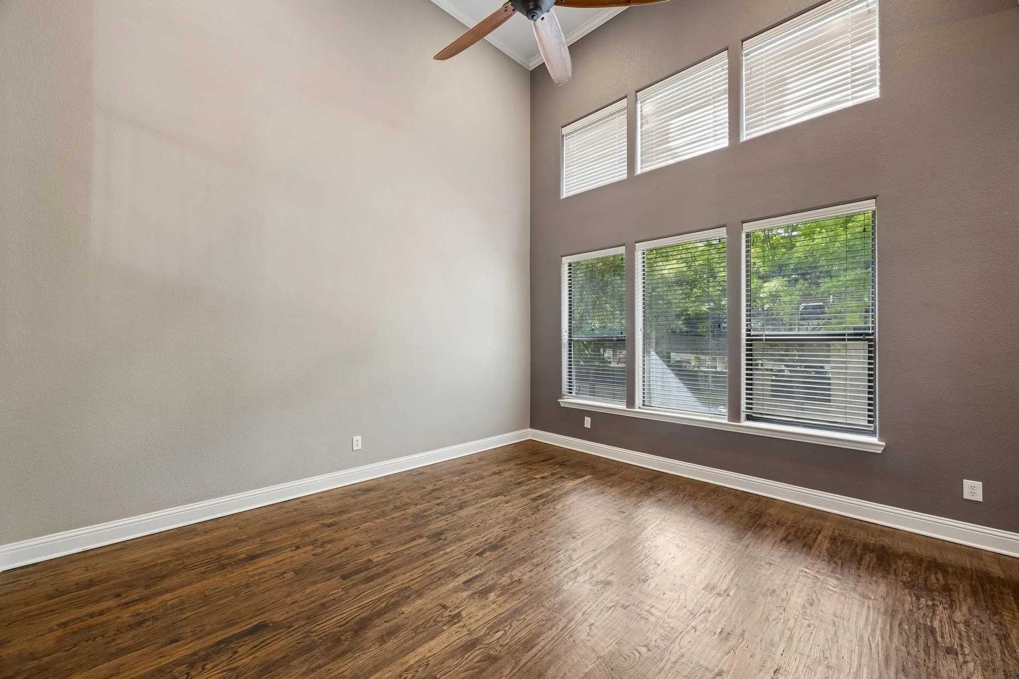 Vaulted ceiling with a ceiling fan, wood-finish flooring, multiple windows with blinds, and white baseboards