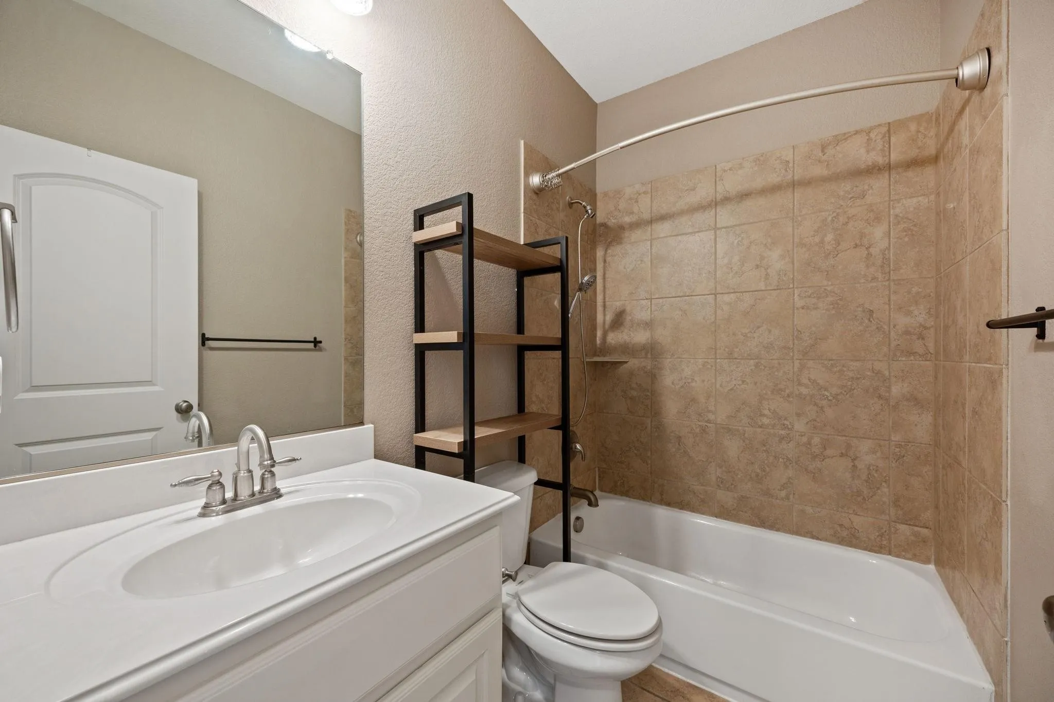 White vanity with an integrated sink and brushed nickel faucet, large wall mirror, and a shower-bathtub combination with ceramic tile surround